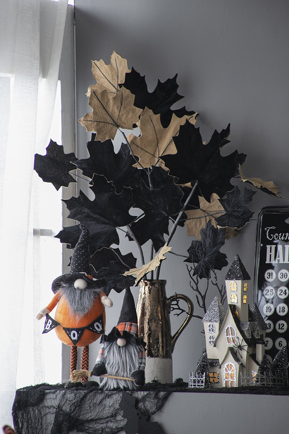 Two Halloween gnomes with witch hats one holding a broom on a mantelpiece