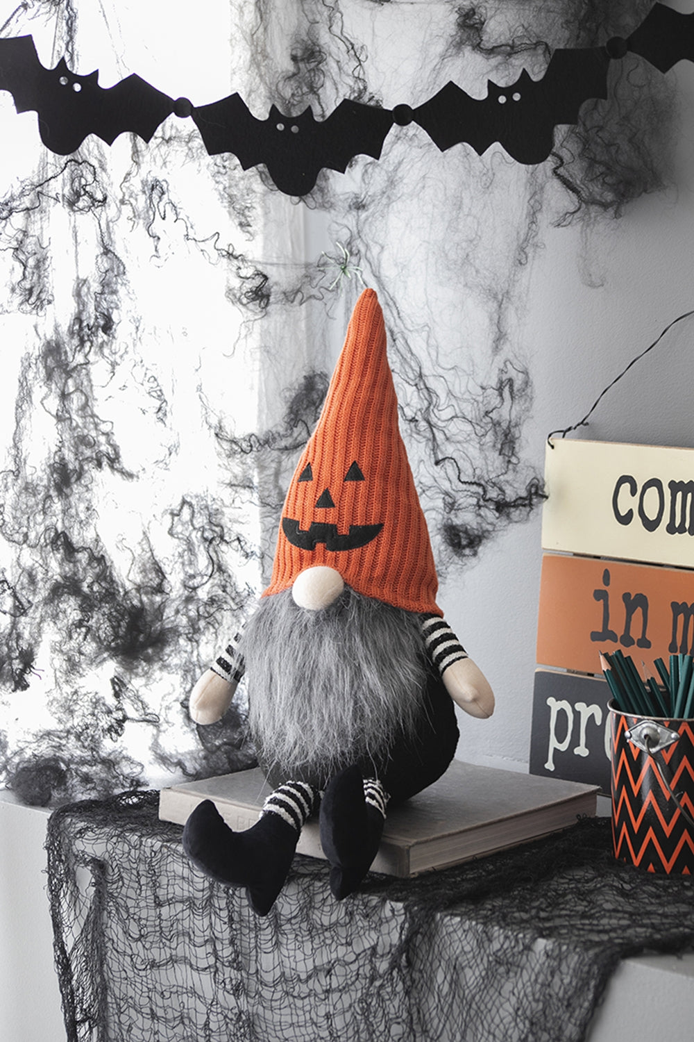 Halloween gnome with orange pumpkin hat and gray beard sitting on book