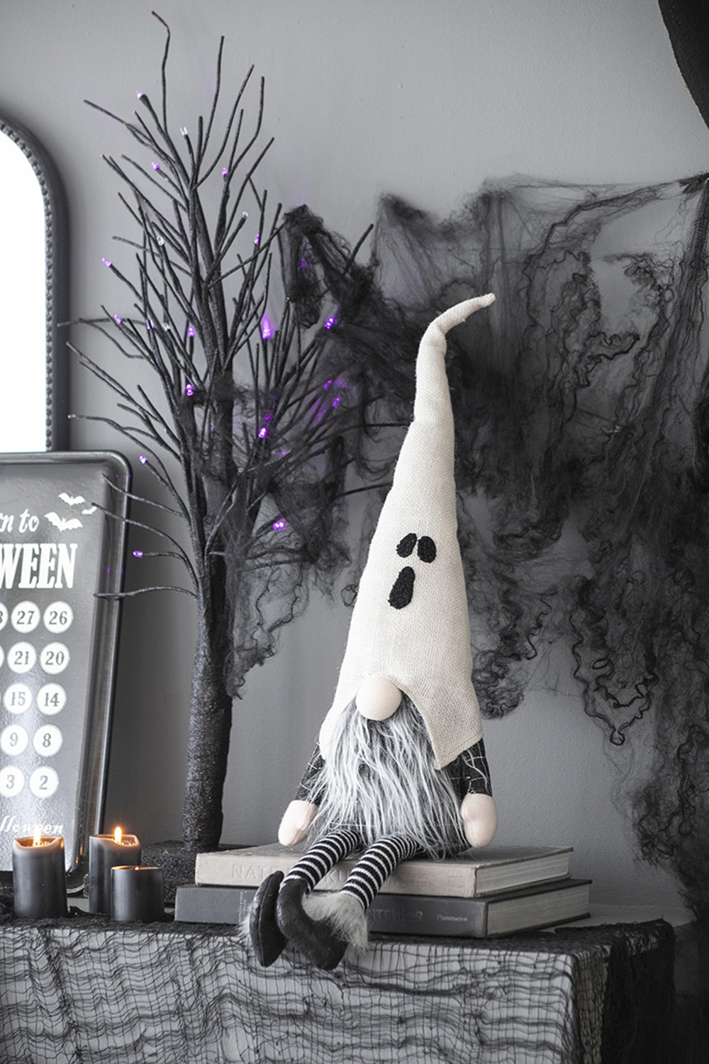 Spooky ghost gnome with long white hat and grey beard sitting on books