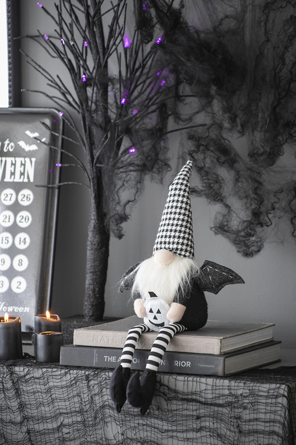 Halloween gnome with black and white patterned hat holding pumpkin sitting on books