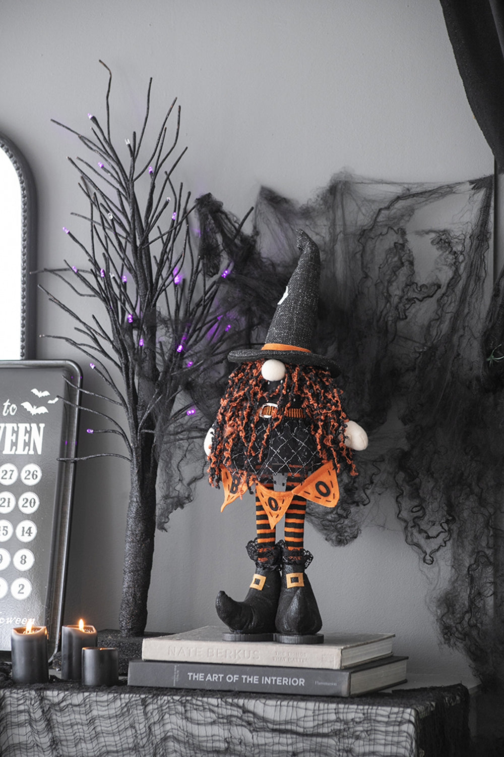 Halloween witch gnome decoration with orange yarn hair and black hat on books