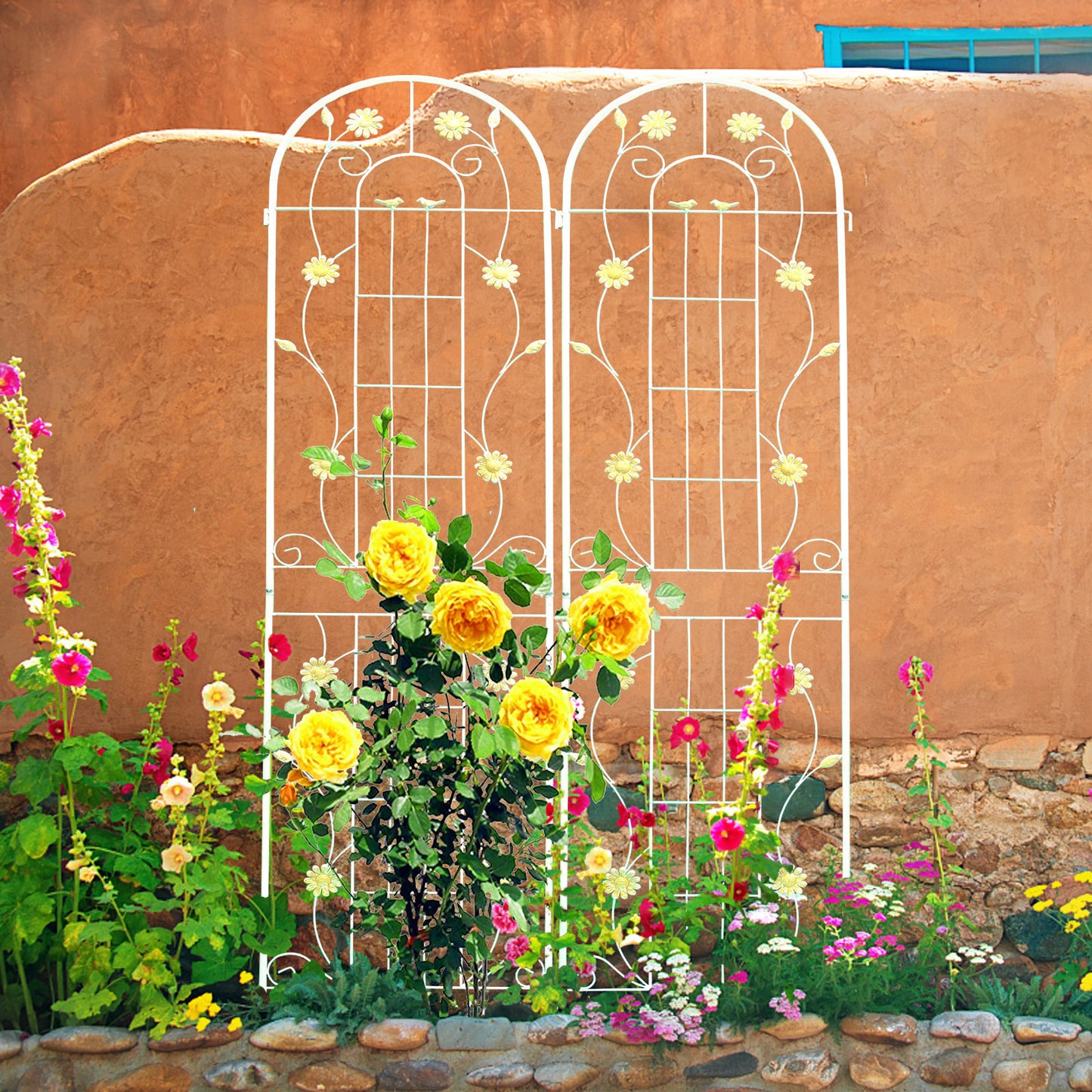 White metal garden trellis with daisy accents supporting yellow roses and hollyhocks