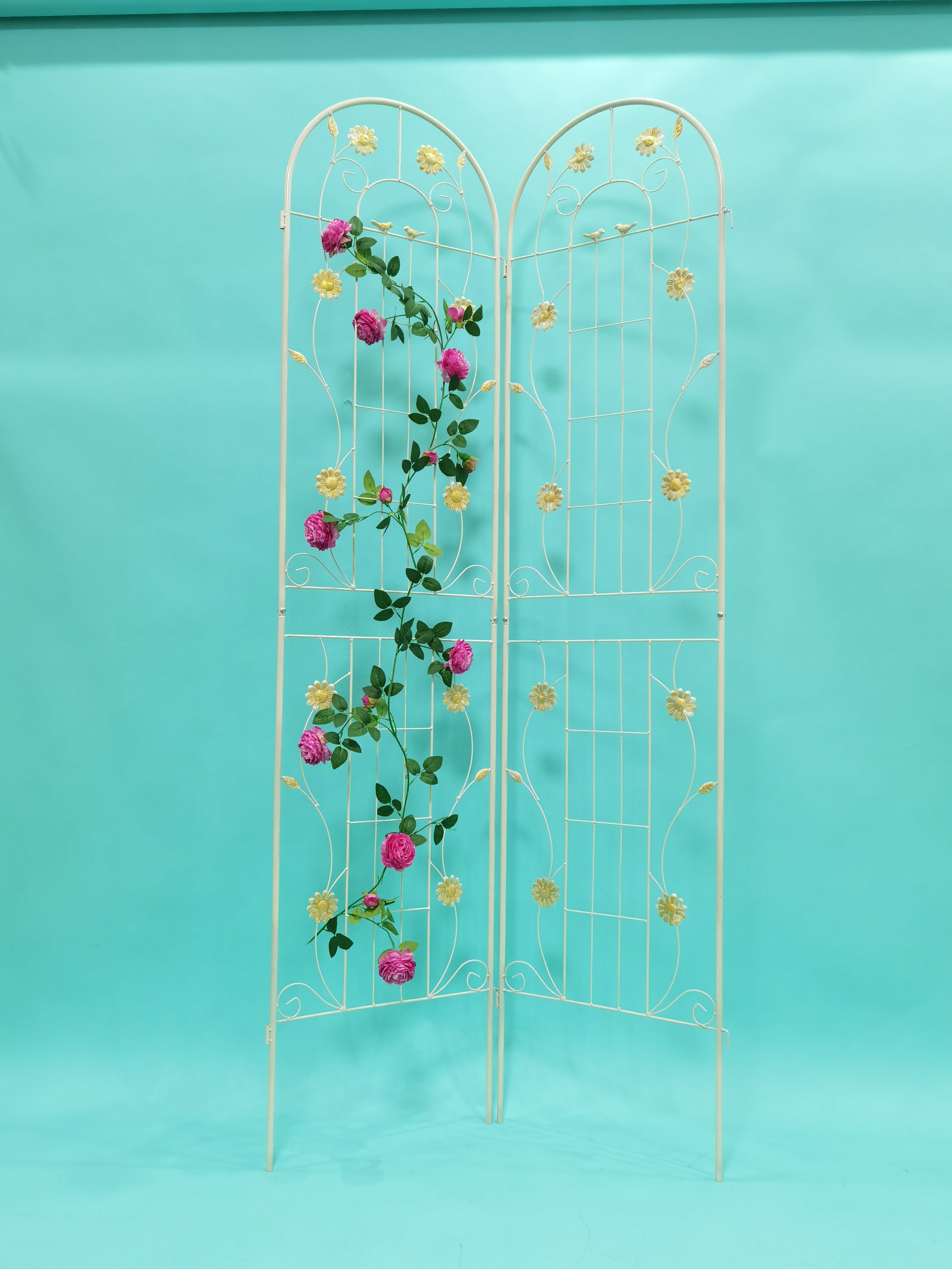 Ornate white metal garden trellis adorned with pink roses and yellow daisies