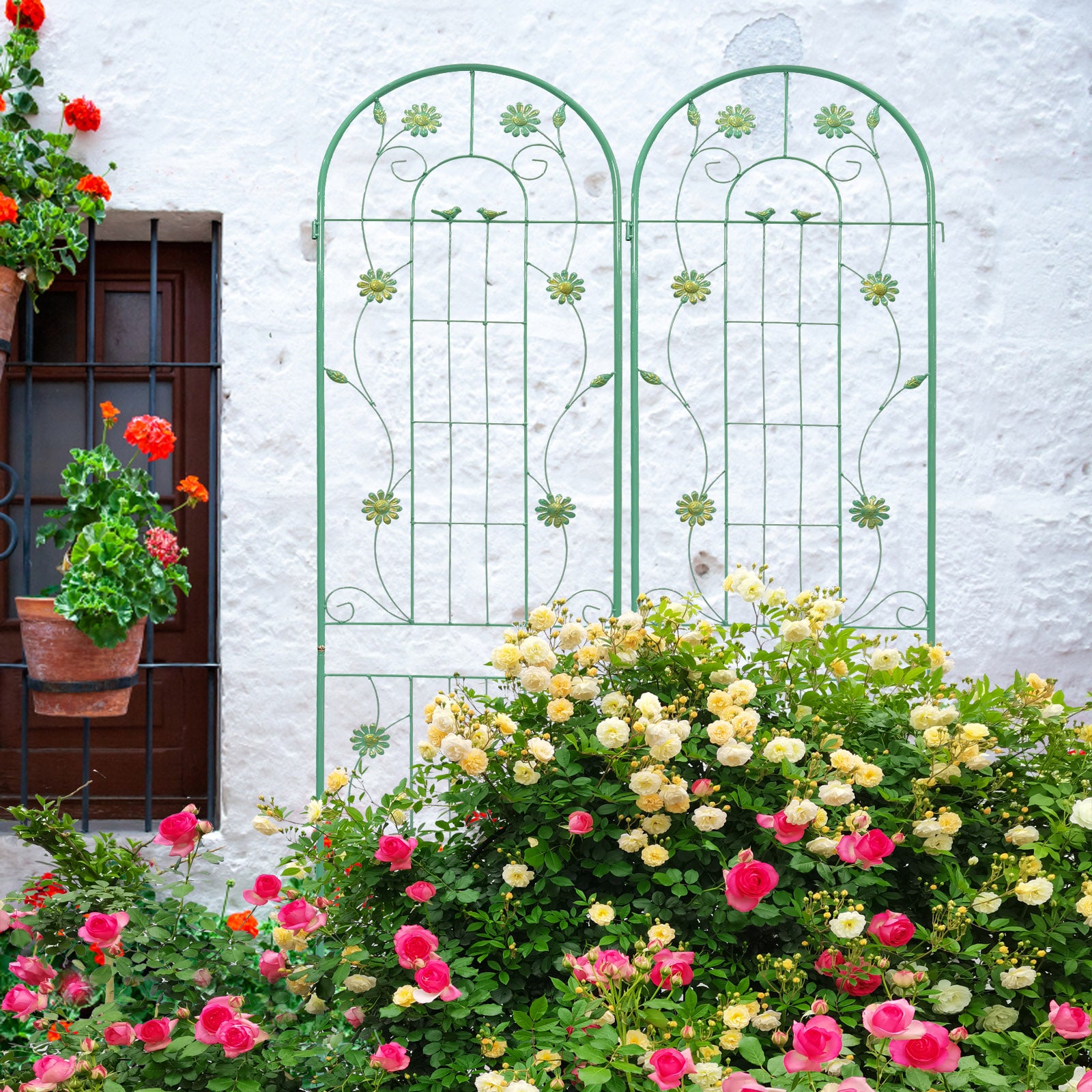 Green metal garden trellis with floral and bird accents framing blooming pink and yellow roses