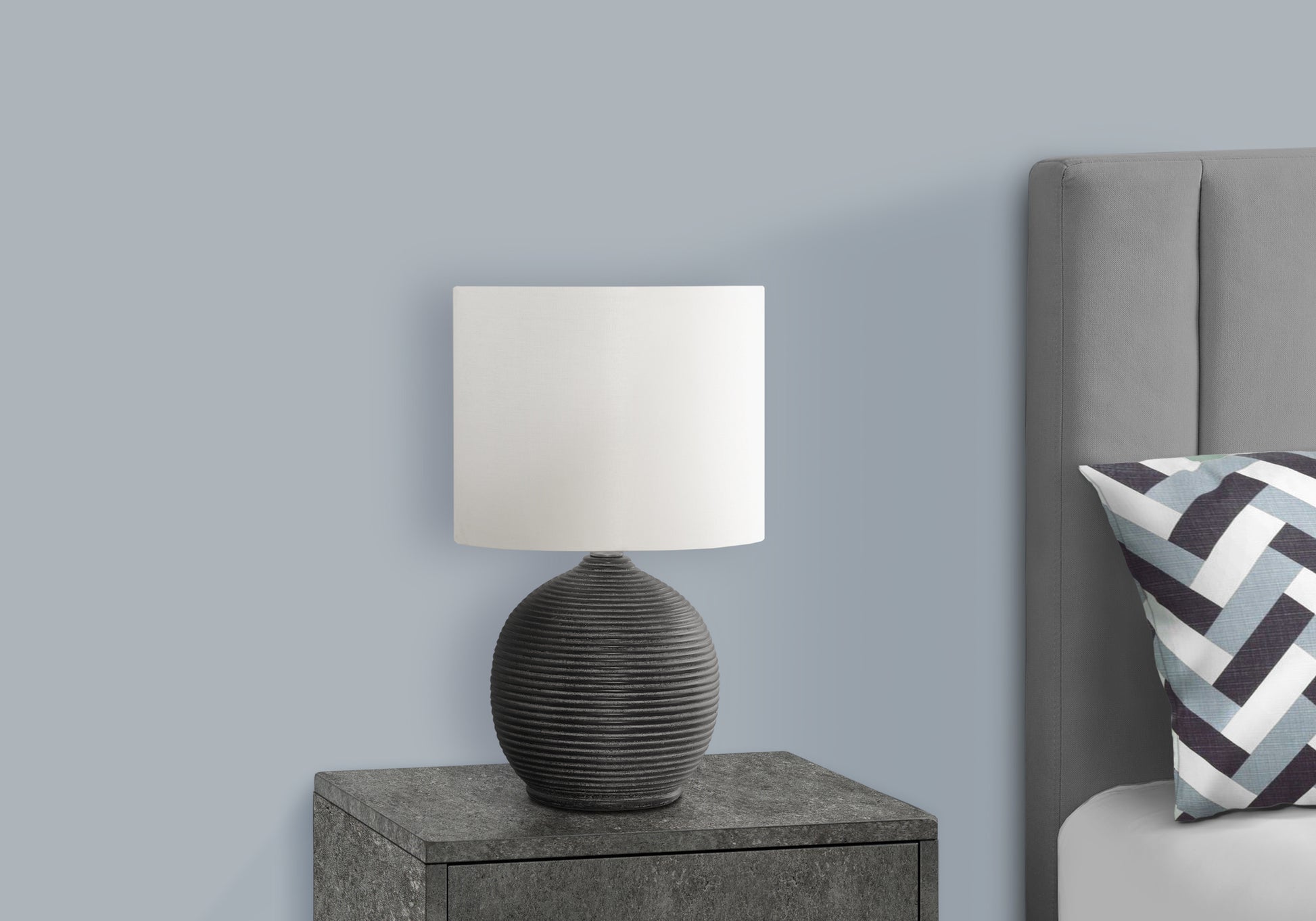 Textured grey ceramic table lamp with white fabric shade on bedside table