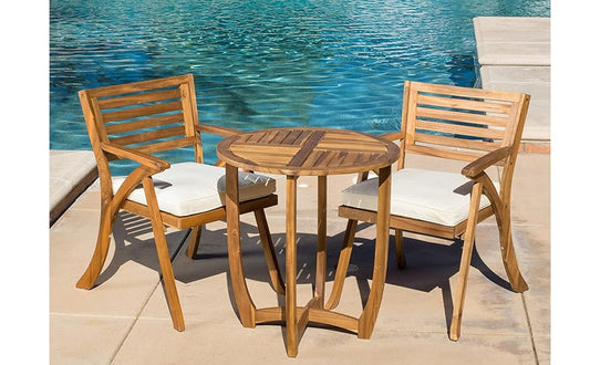 Wooden patio bistro set with white cushions by a pool