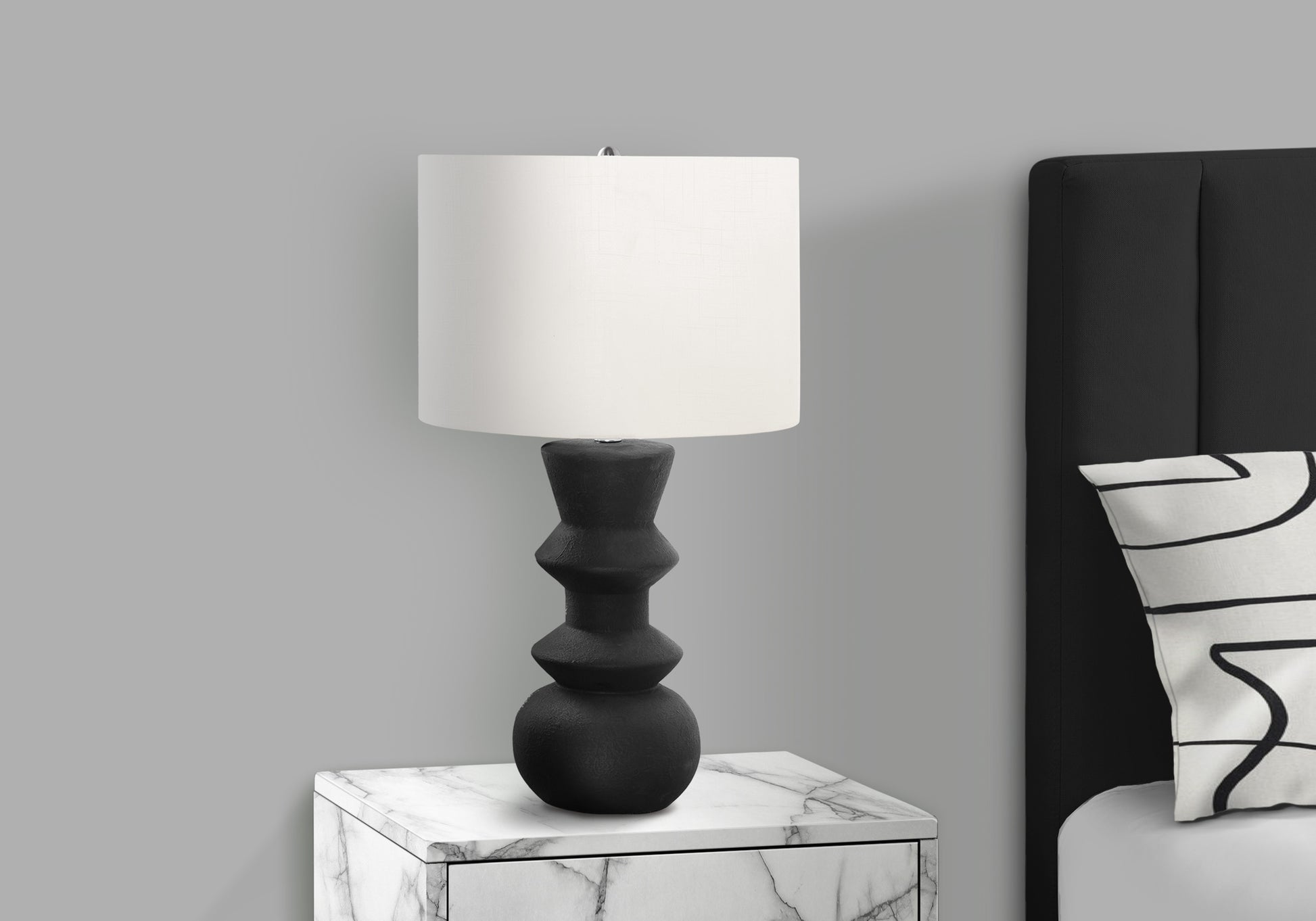 Black sculpted table lamp with white drum shade on marble nightstand