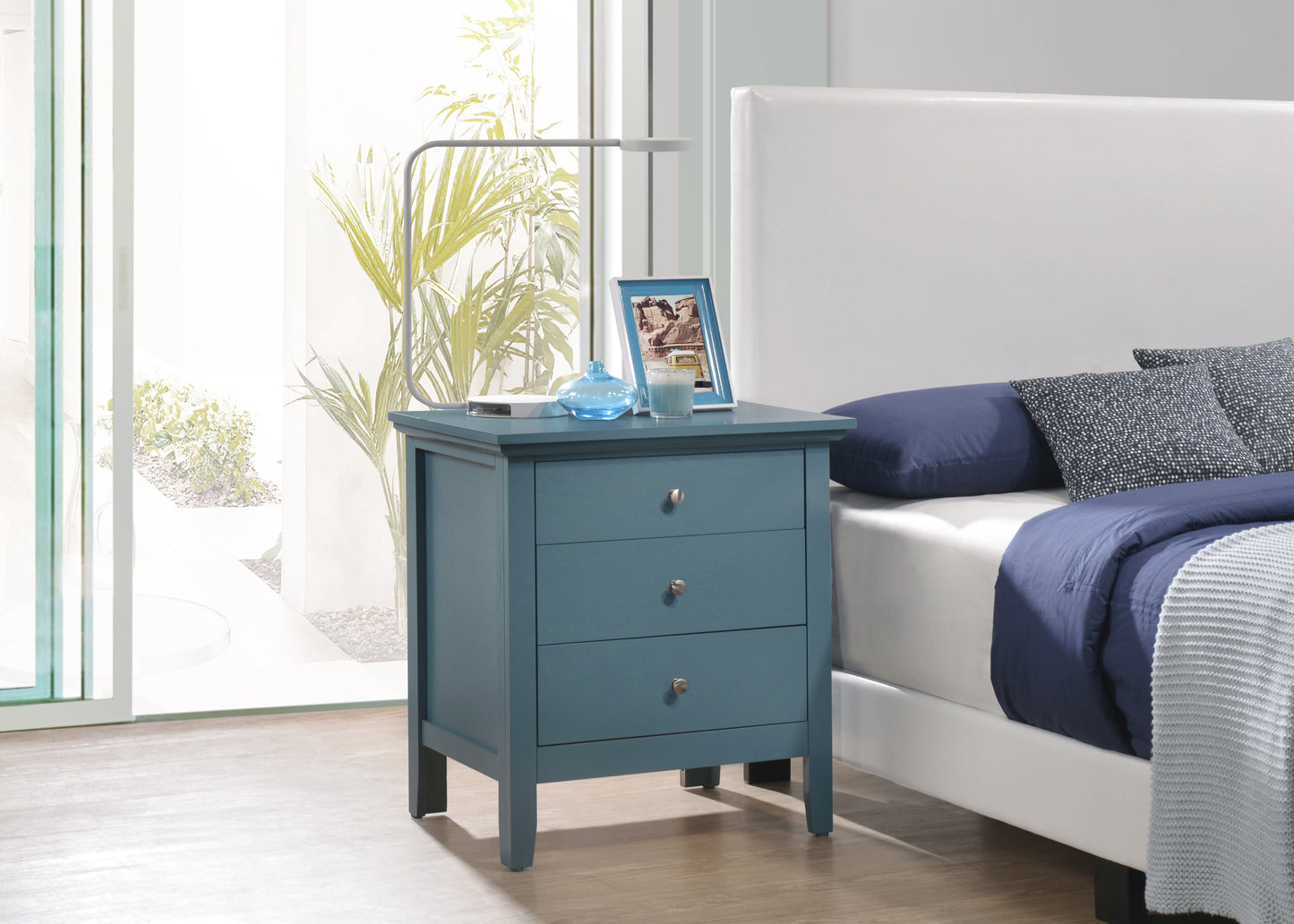 Teal wood nightstand with three drawers and silver knobs next to a bed