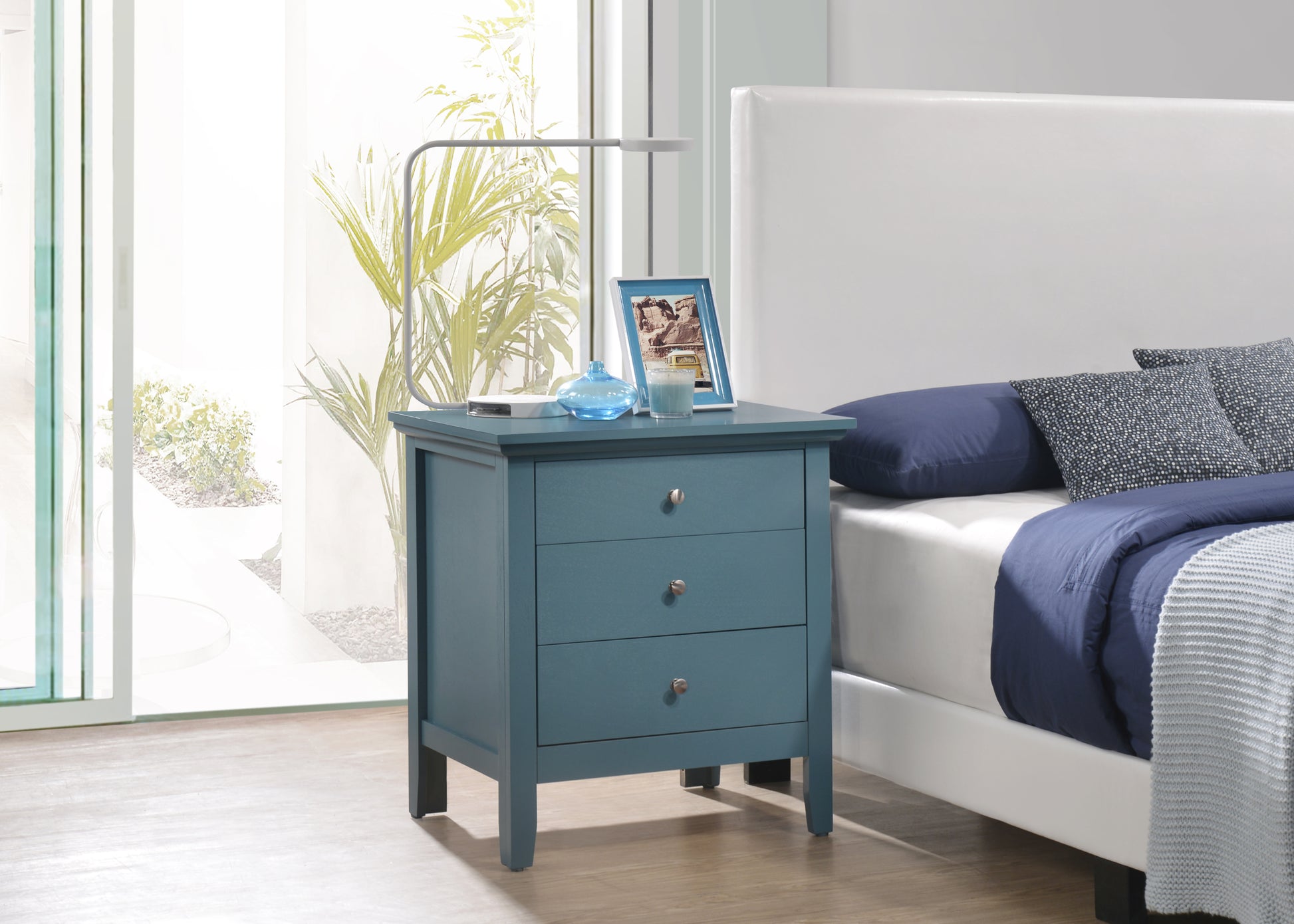 Teal wood nightstand with three drawers and silver knobs next to a bed