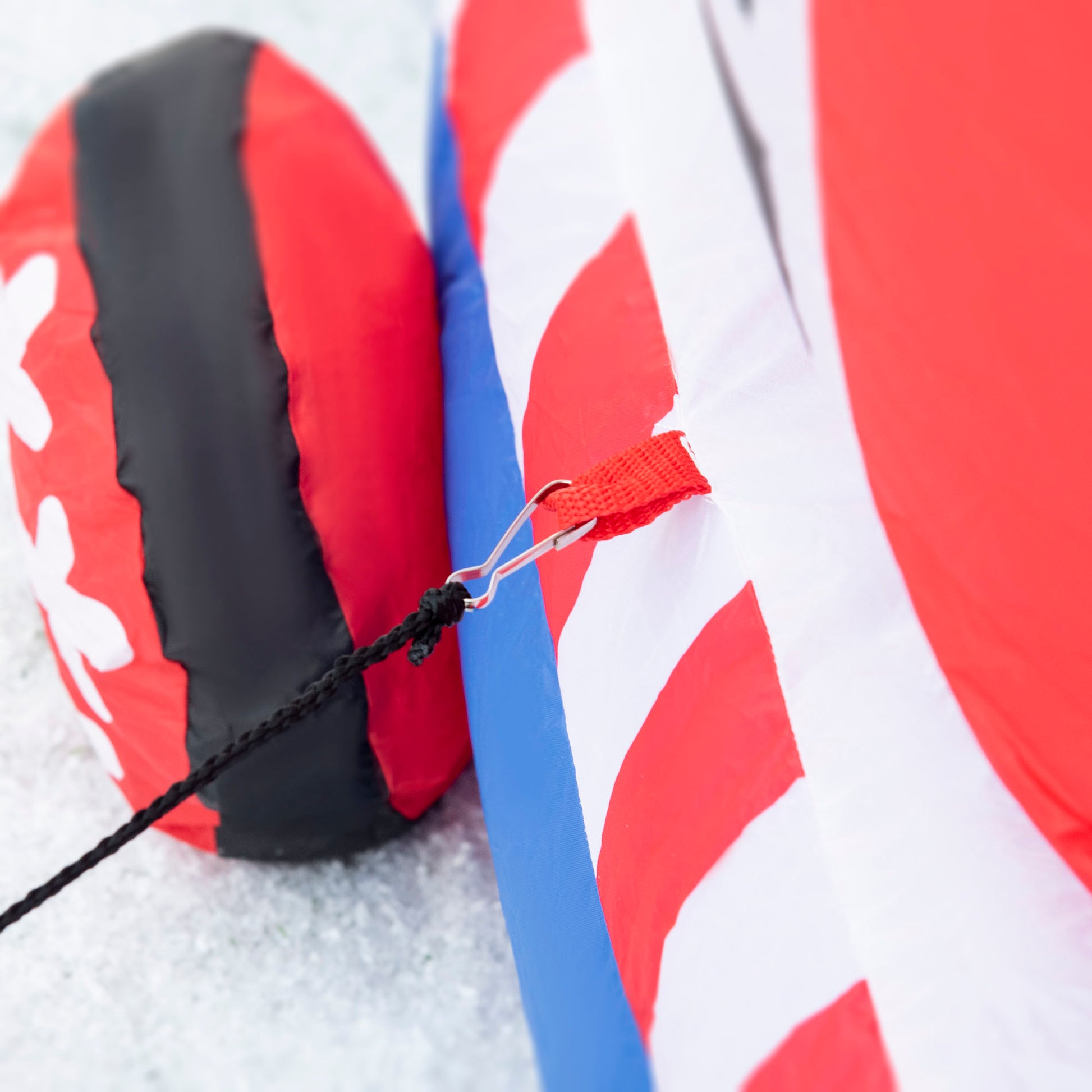 Closeup of an inflatable snowman base tether point with a red fabric loop and metal clip