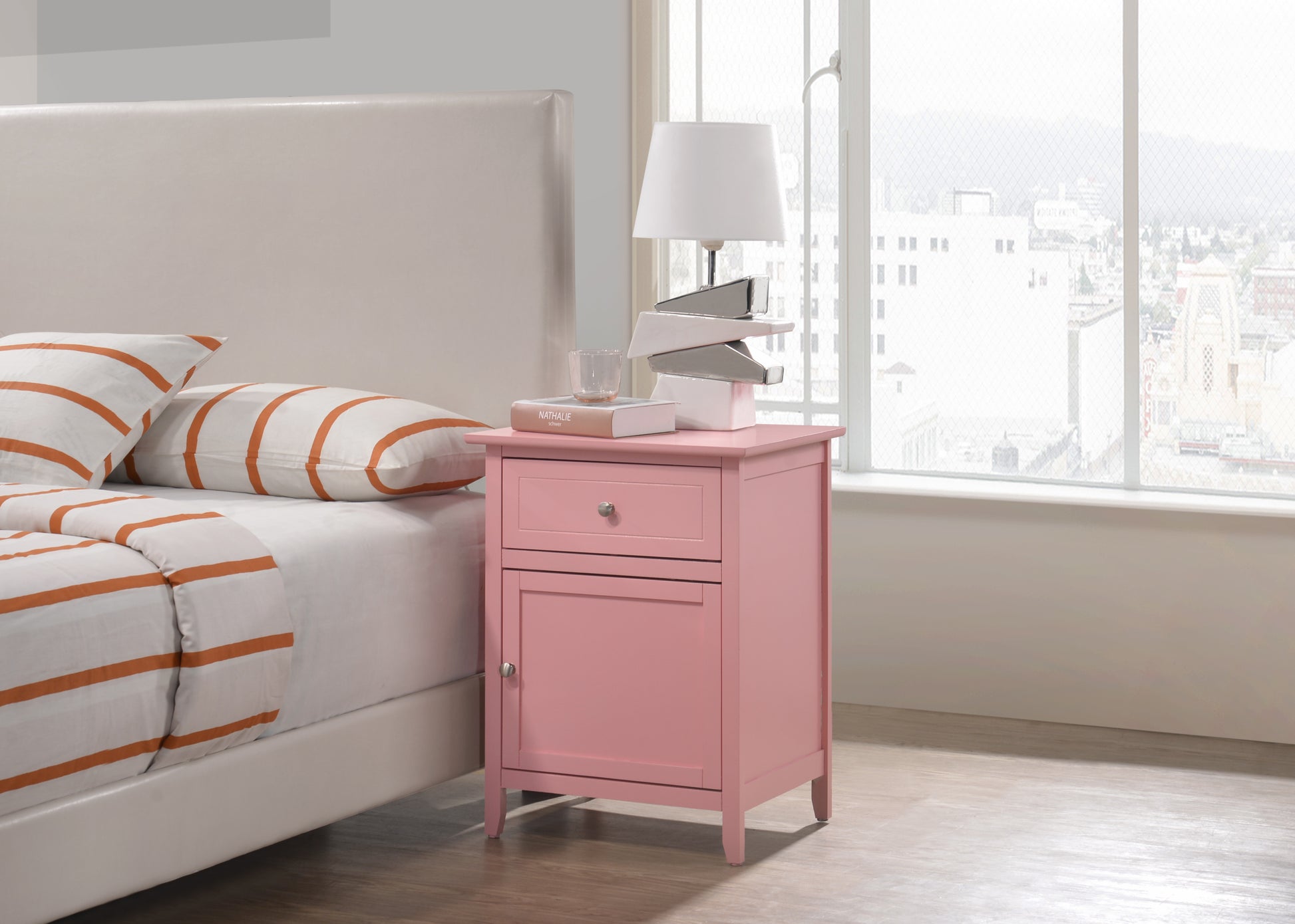 Pink wooden bedside table with one drawer and one cabinet next to a bed