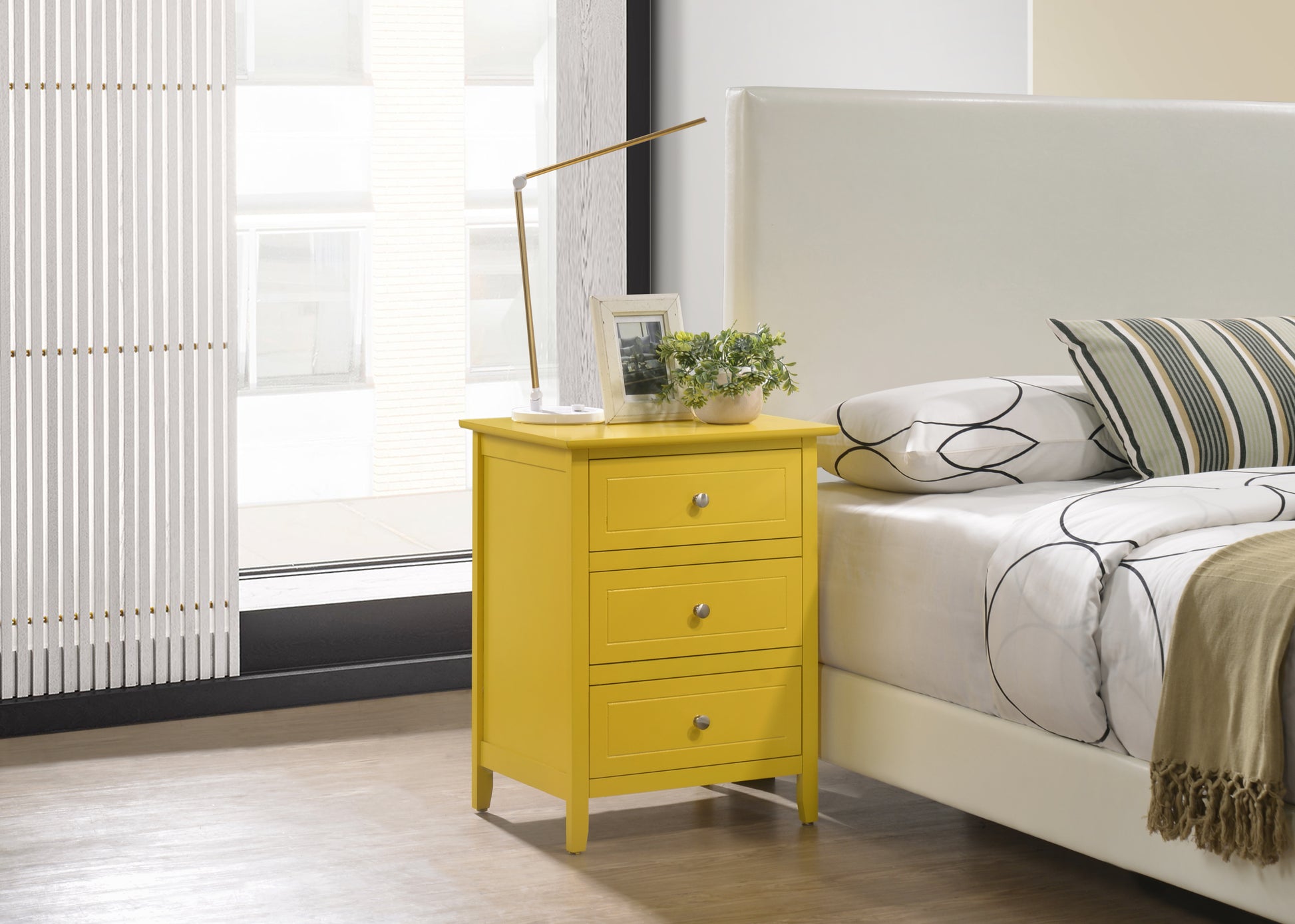 Yellow threedrawer nightstand with silver knobs beside a bed