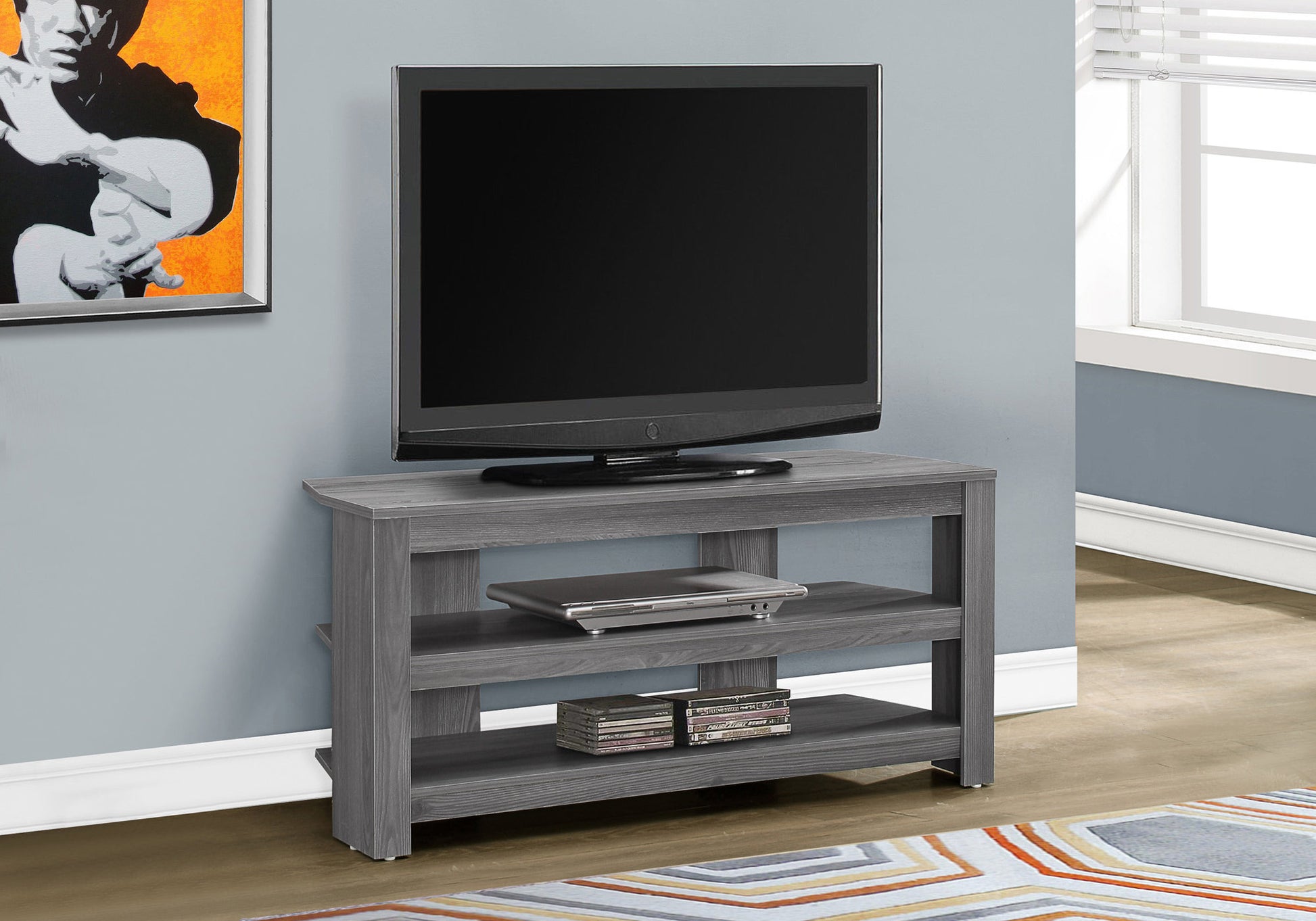 Gray wood media console with open shelves holding a laptop and DVDs