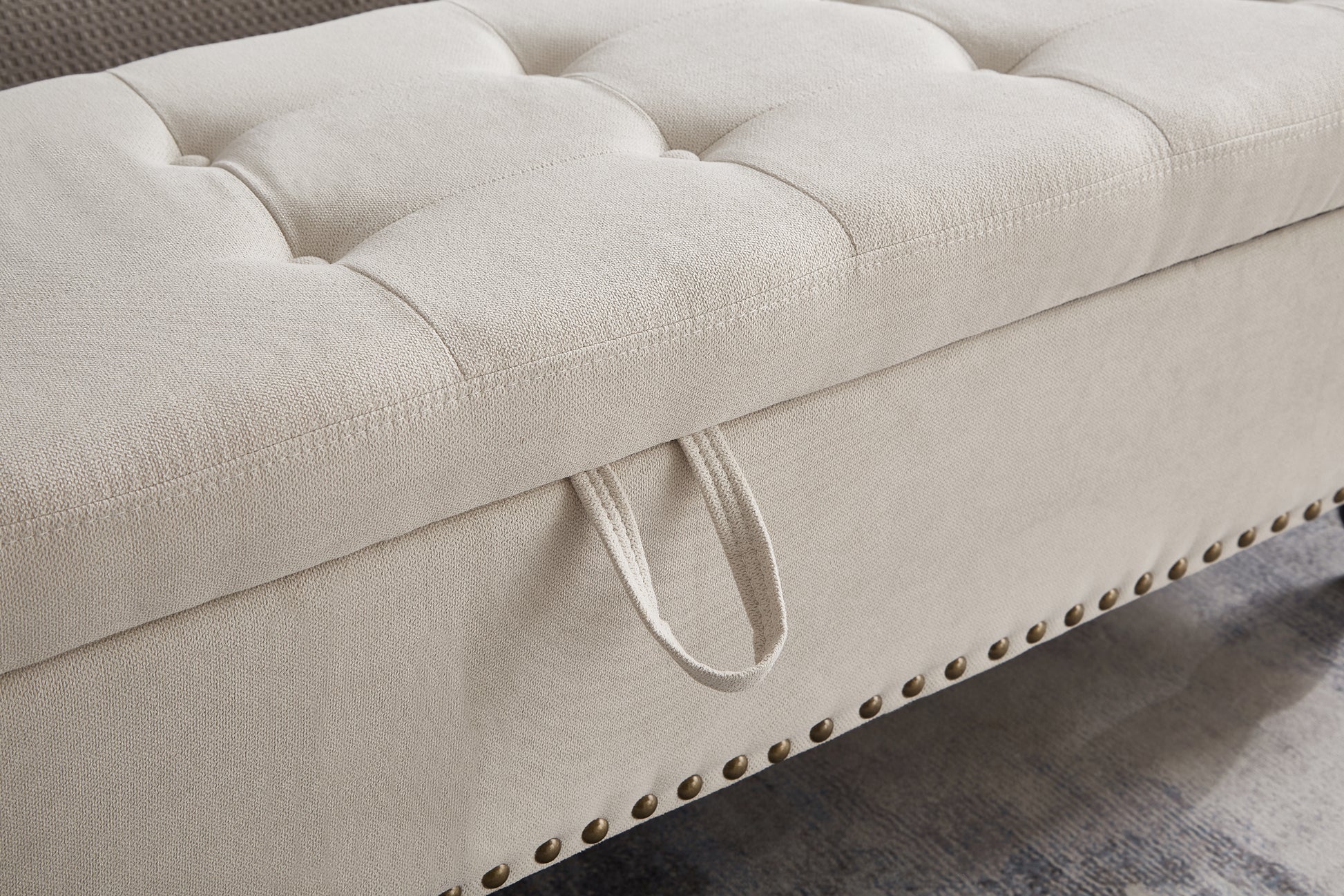 Beige linen tufted storage ottoman with brass nailhead trim and pull loop