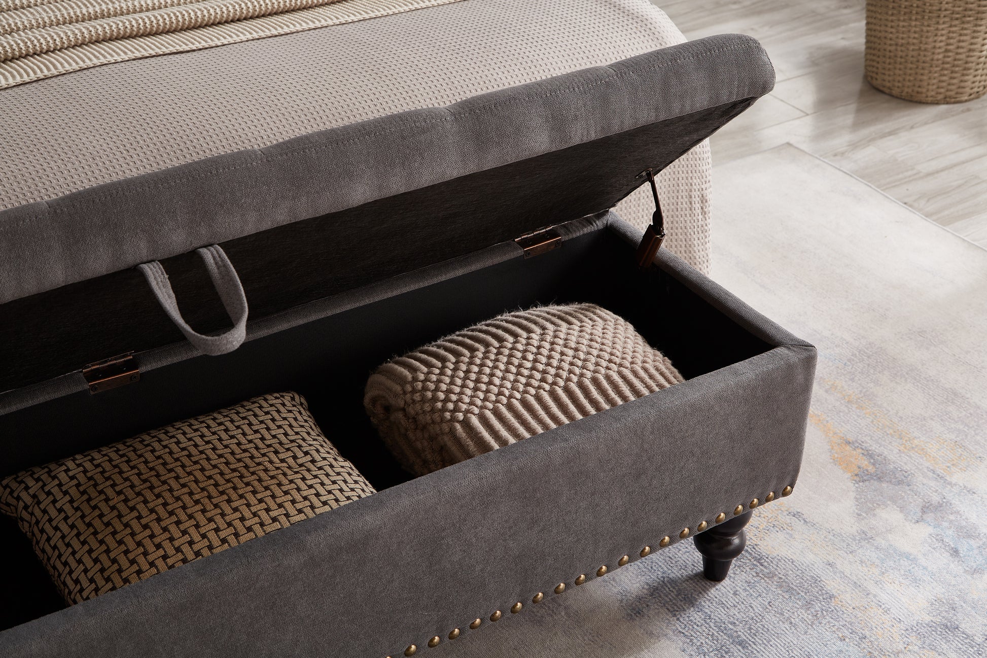 Gray upholstered storage bench with brass nailhead trim and plush pillows inside