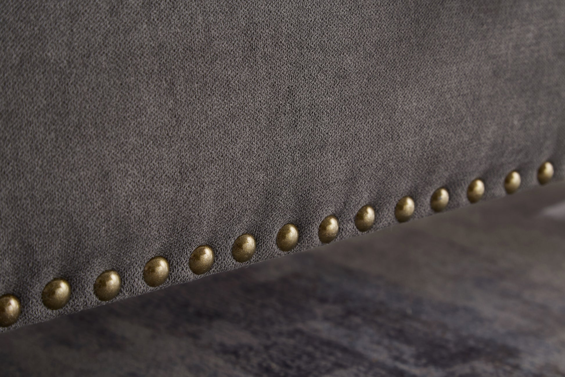 Closeup of grey fabric upholstery with brass nailhead trim detail