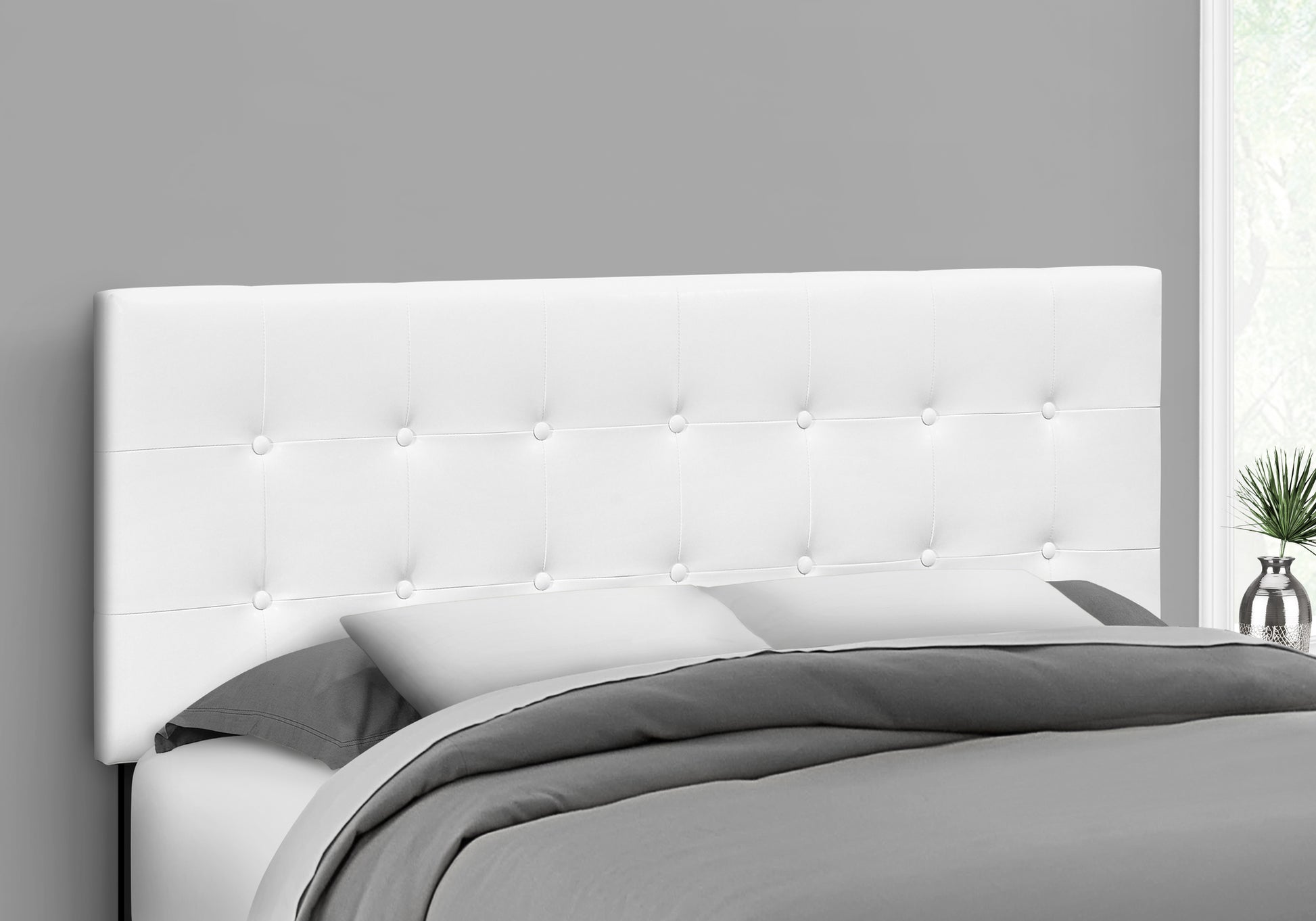 White faux leather tufted headboard on a bed with gray bedding