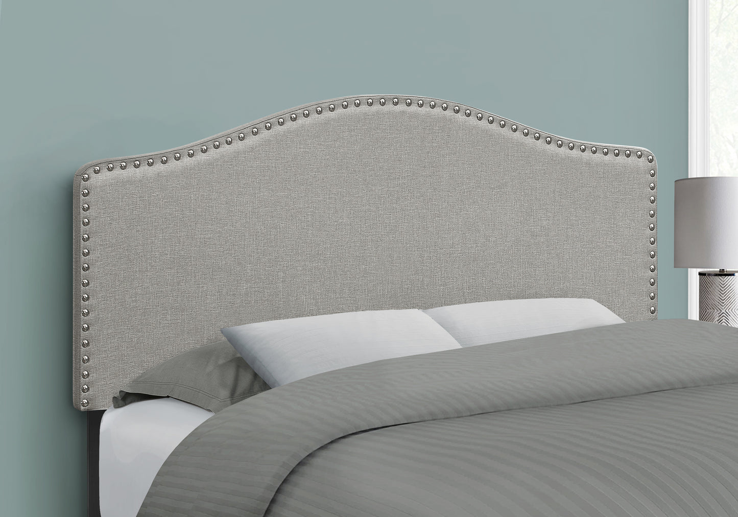 Arched grey upholstered headboard with silver nailhead trim on a bed