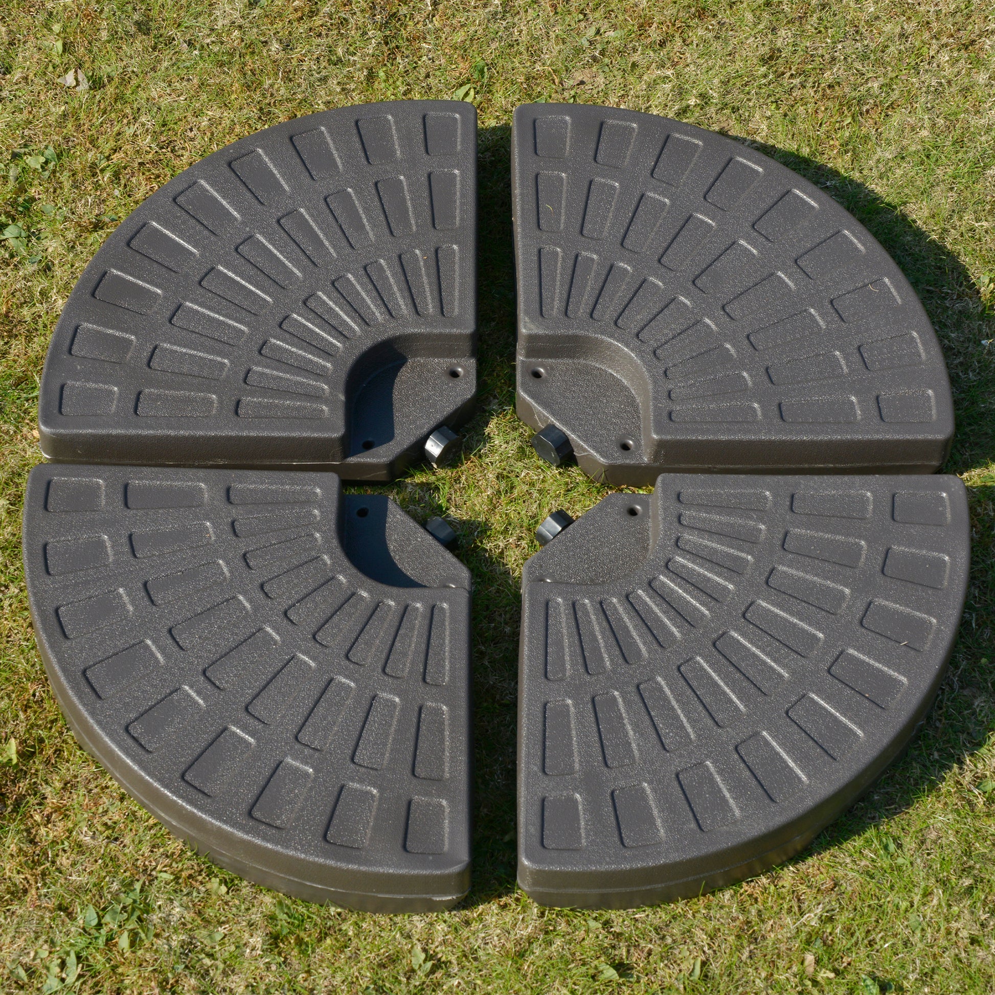 Four dark grey quartercircle patio umbrella bases with textured surface on grass