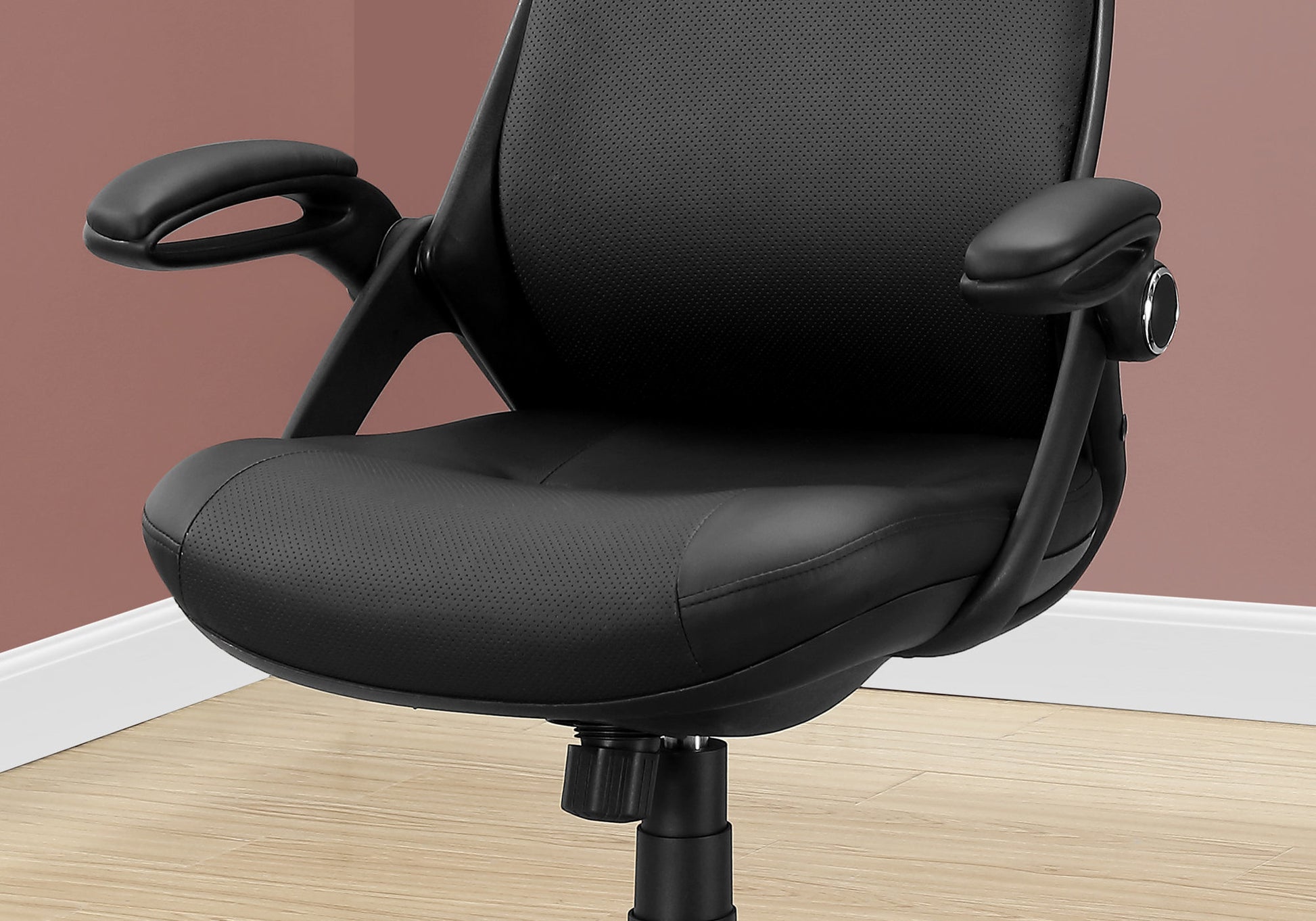 Closeup of a black executive office chair seat with perforated detailing and adjustable armrests