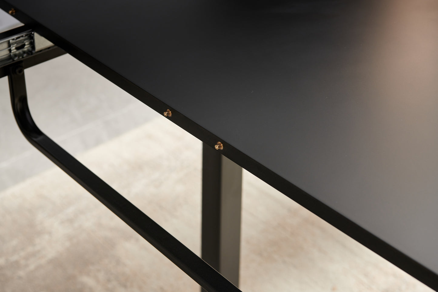 Closeup of a matte black desk with silver drawer slides and gold screws