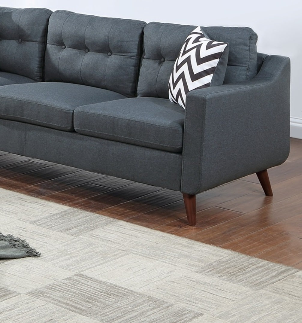 Dark gray tufted fabric sofa with midcentury modern style wooden legs and a chevron pillow