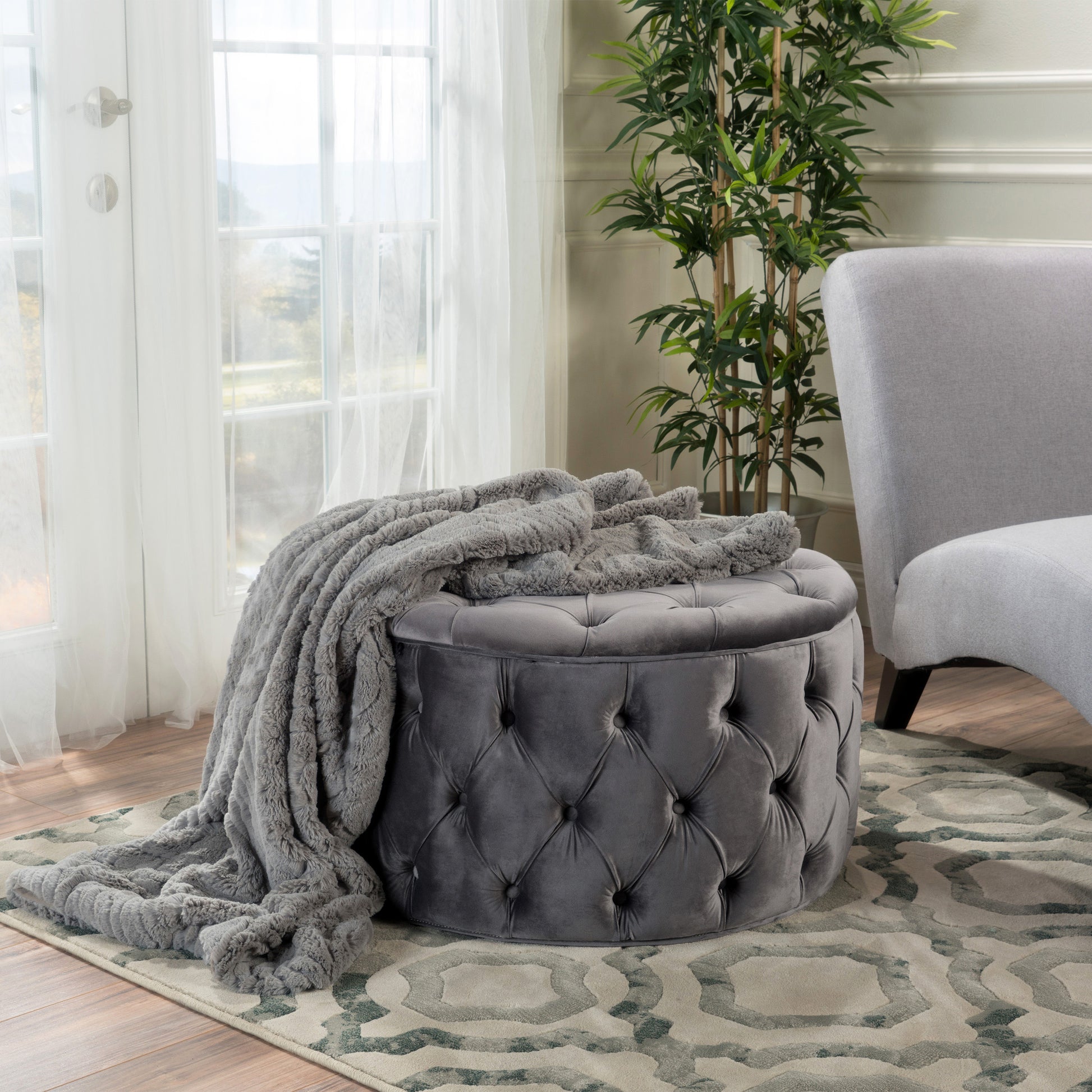 Gray tufted velvet ottoman with a plush faux fur throw draped over it