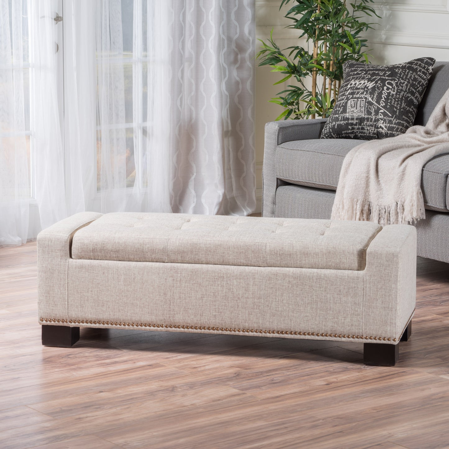 Beige linen storage ottoman with tufted top and brass nailhead trim