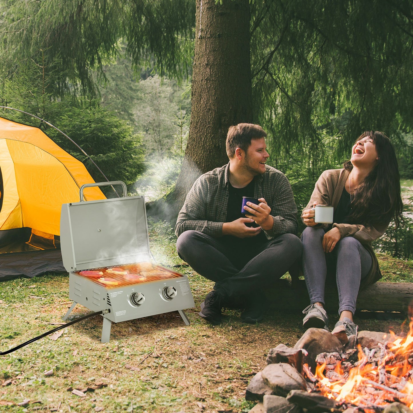 Compact silver portable grill cooking steaks outdoors next to tent