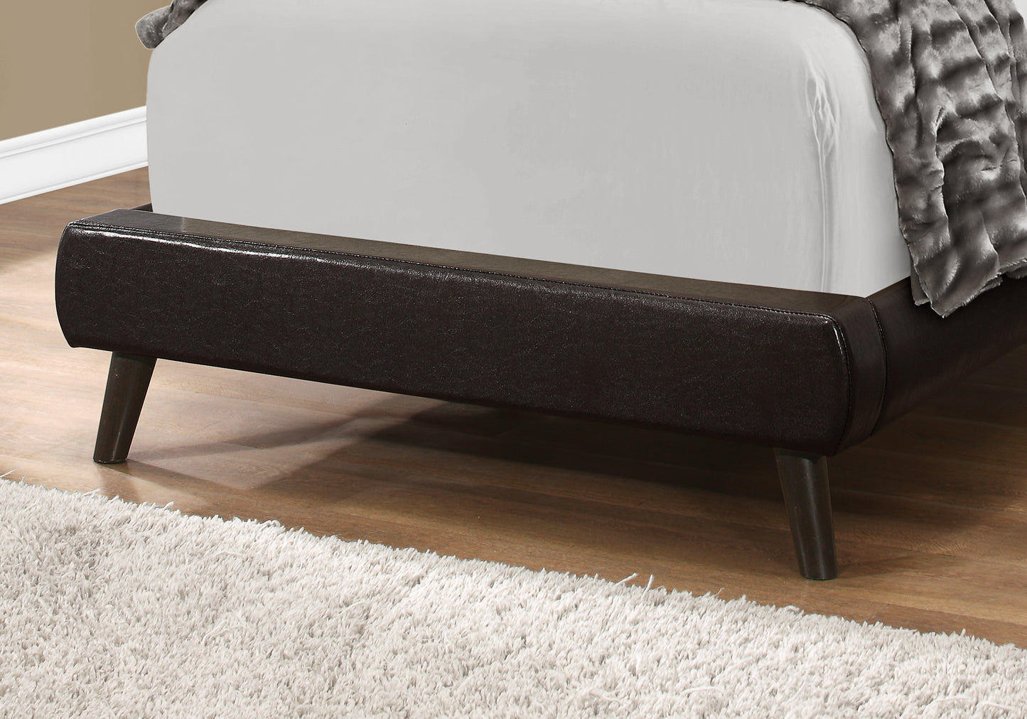 Dark brown faux leather bed frame with angled wooden legs and plush white rug