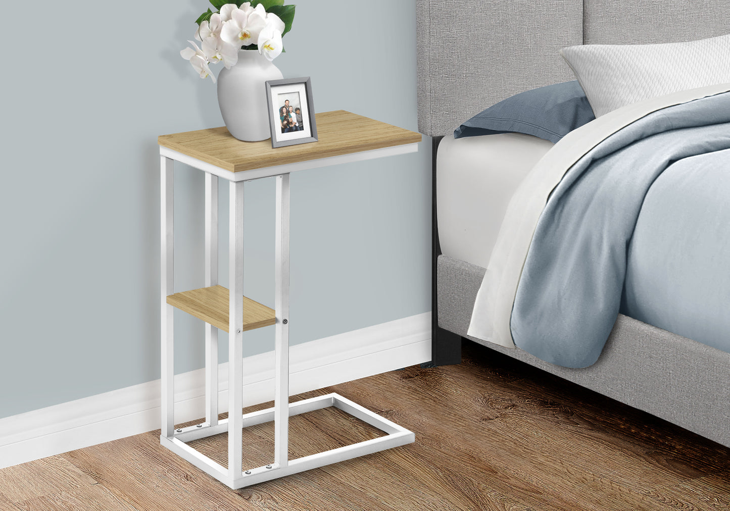 Modern ctable with wood top and white metal frame beside a bed