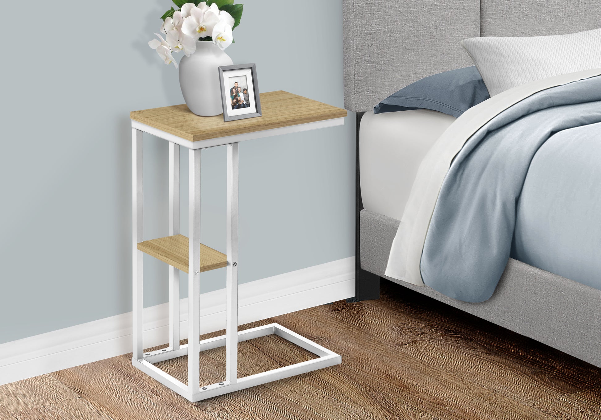 Modern ctable with wood top and white metal frame beside a bed