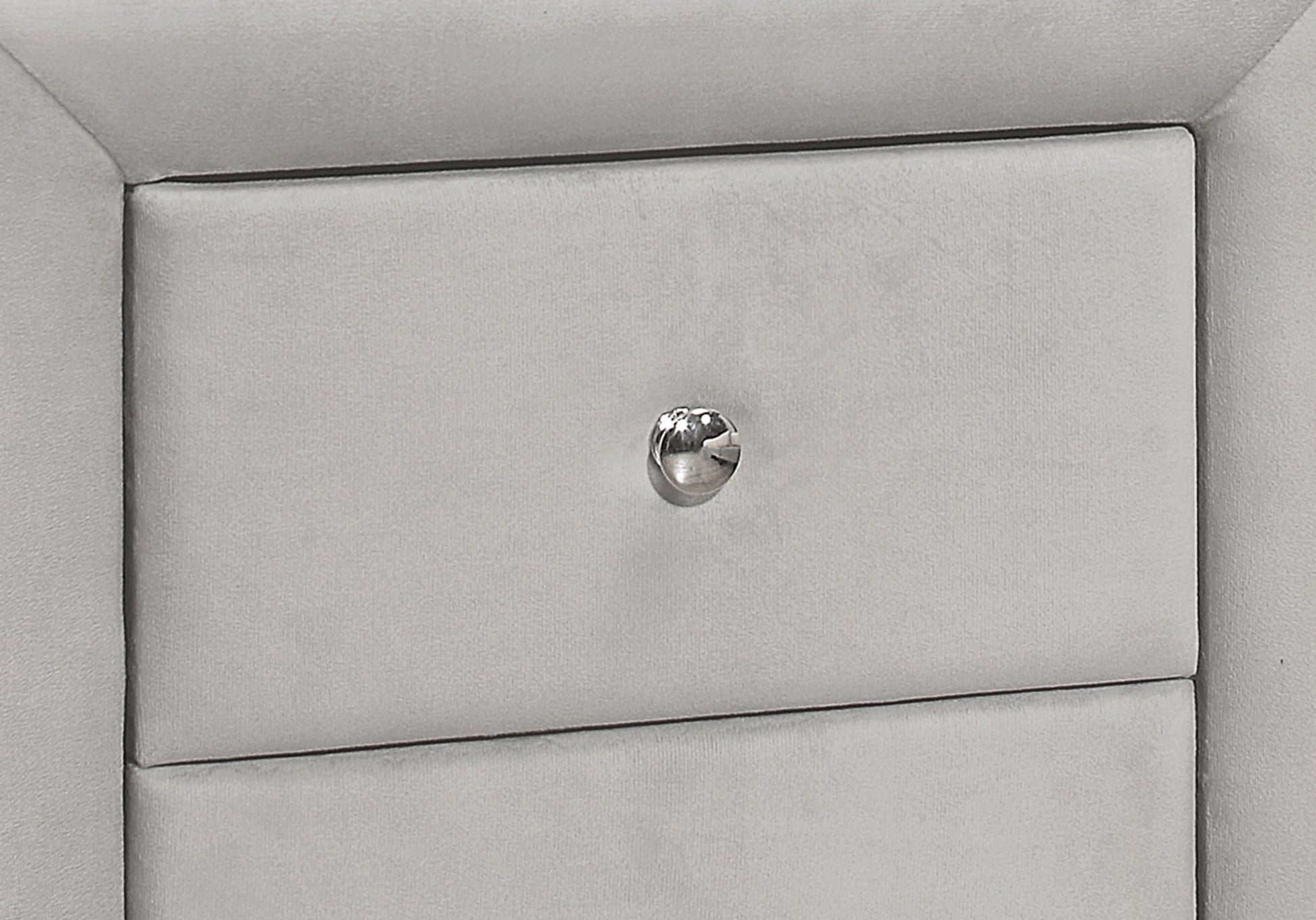 Closeup of a light grey velvet upholstered drawer front with a crystal knob