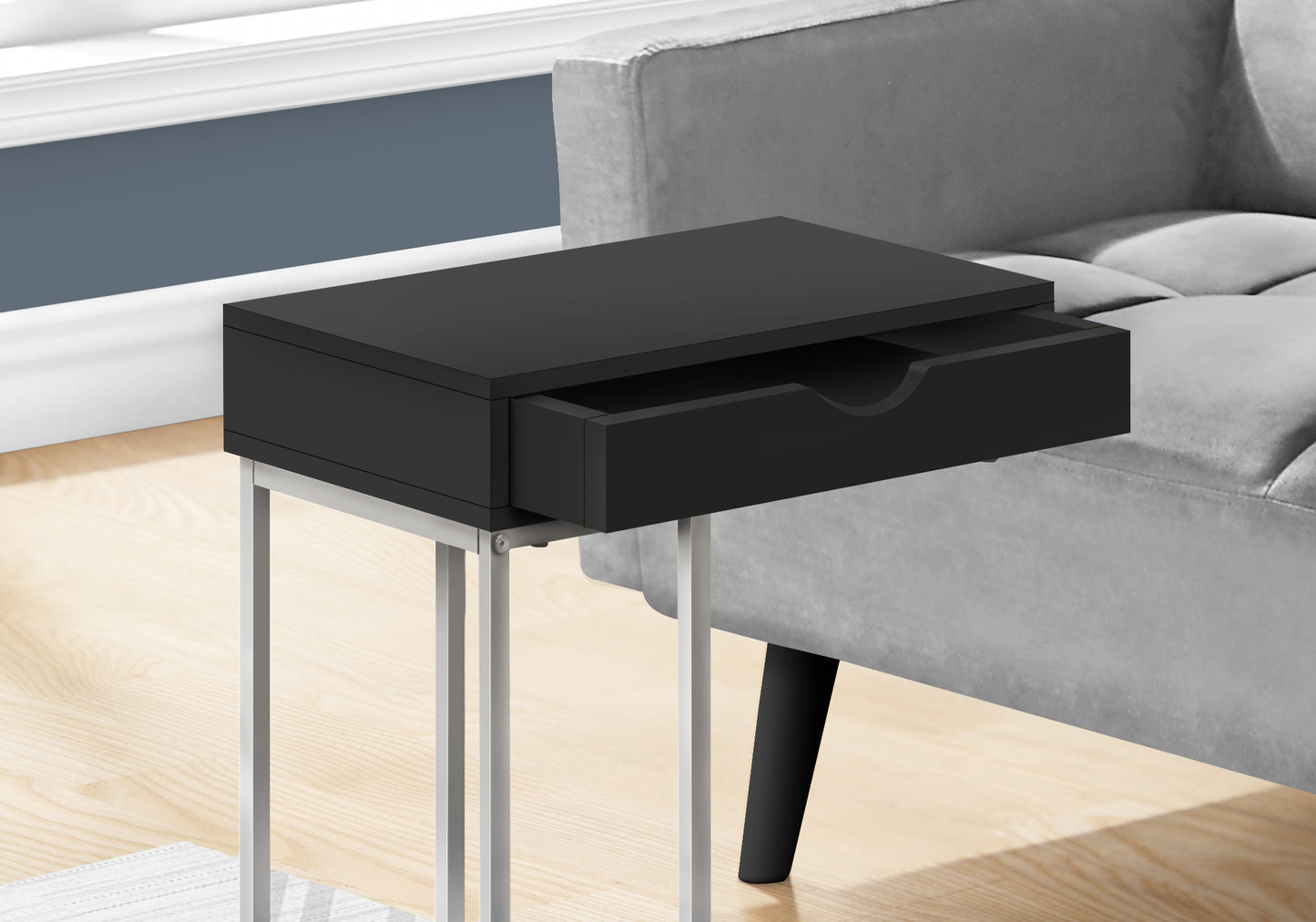 Sleek black end table with open drawer and silver metal legs beside a grey sofa