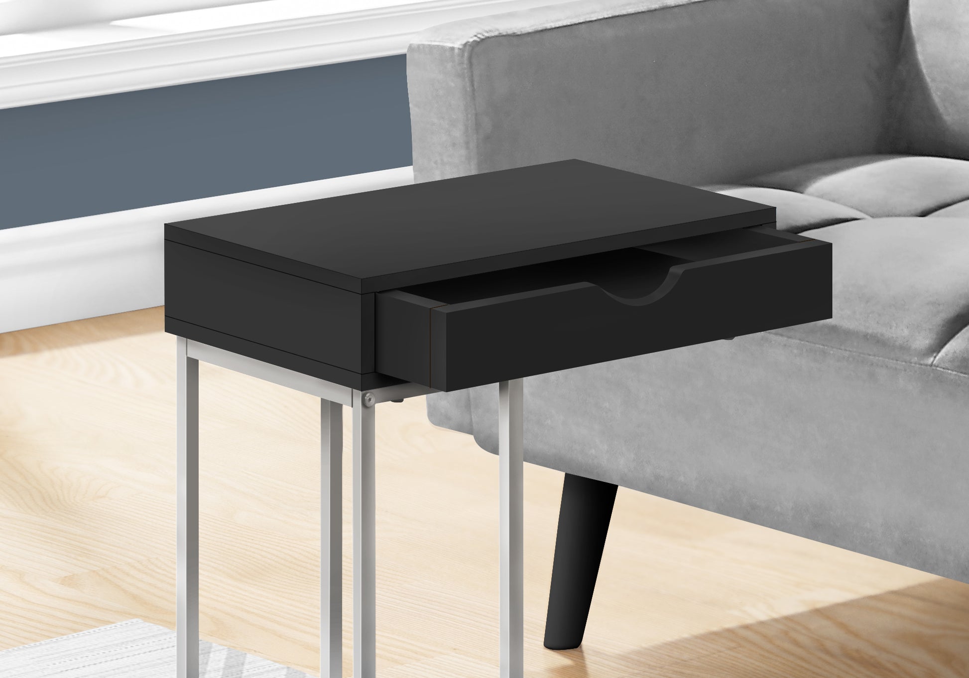Sleek black end table with open drawer and silver metal legs beside a grey sofa