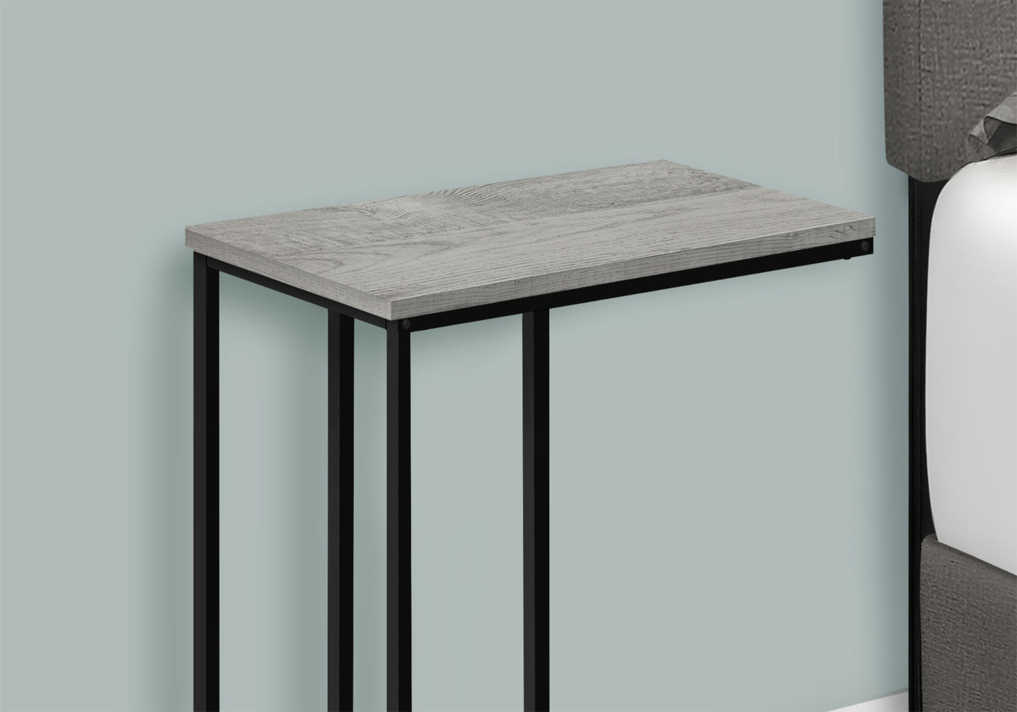 Gray wood grain accent table with black metal frame beside a bed