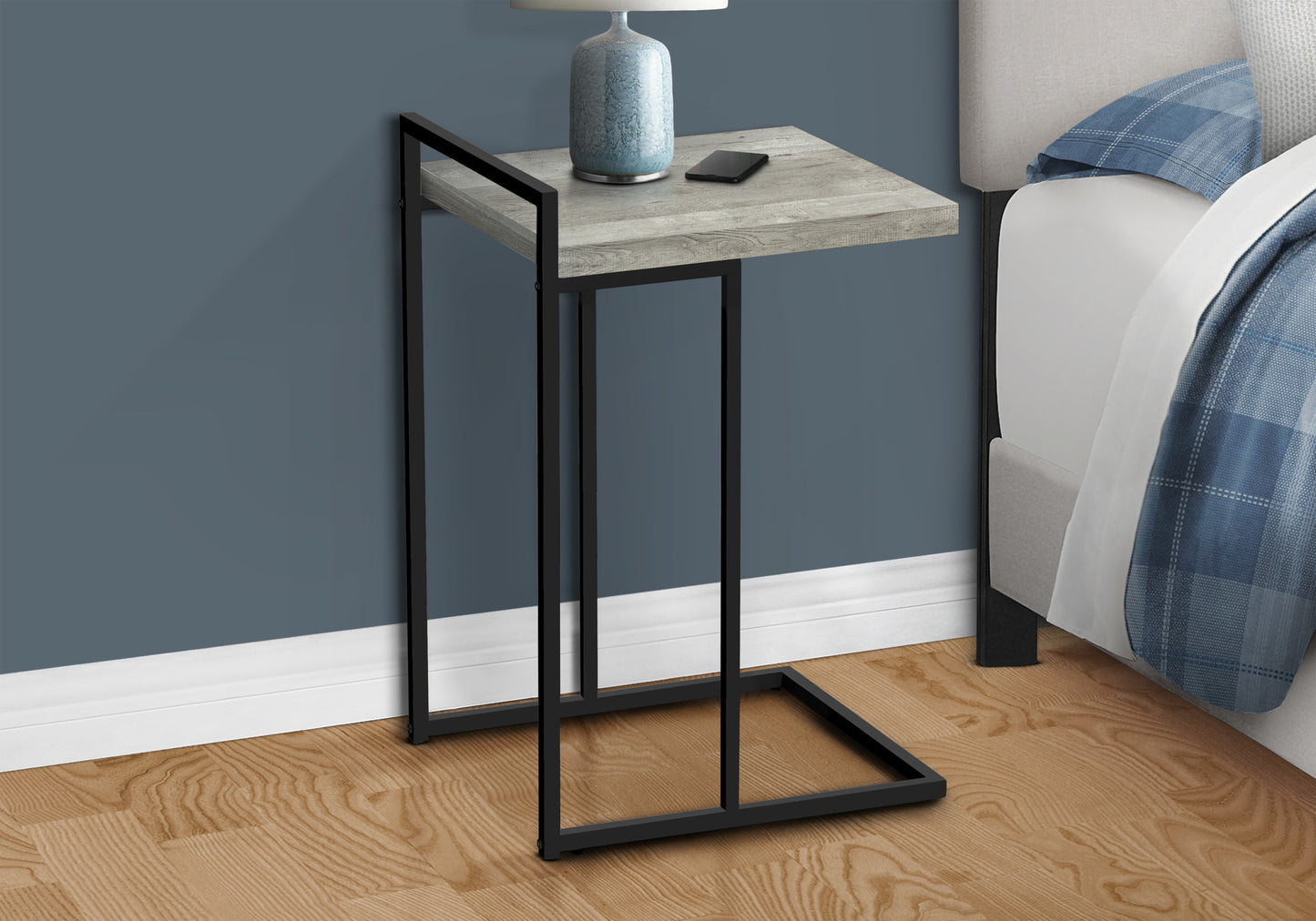 Modern Ctable with gray wood top and black metal frame next to a bed