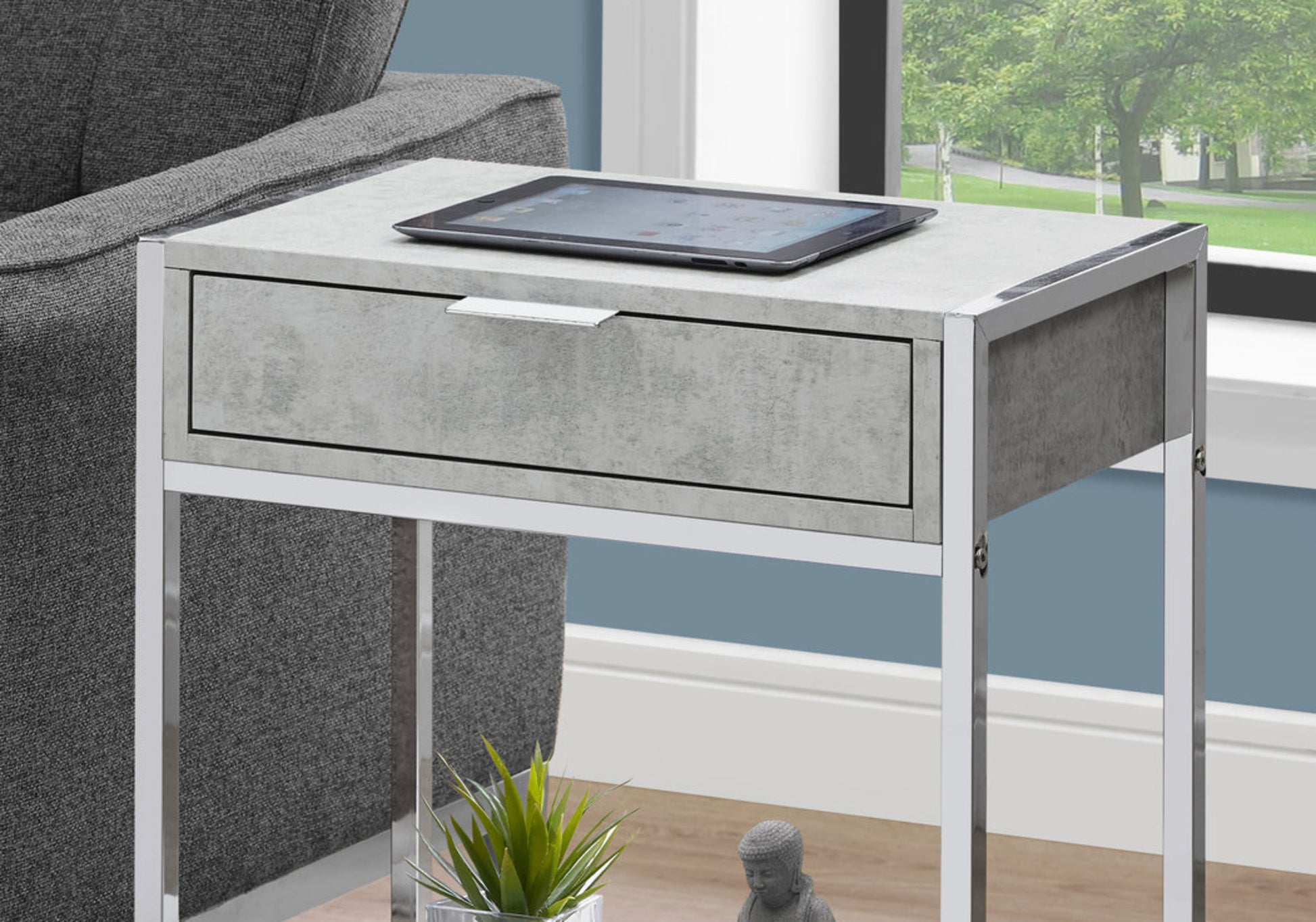 Gray concrete effect end table with silver frame and drawer holding a tablet