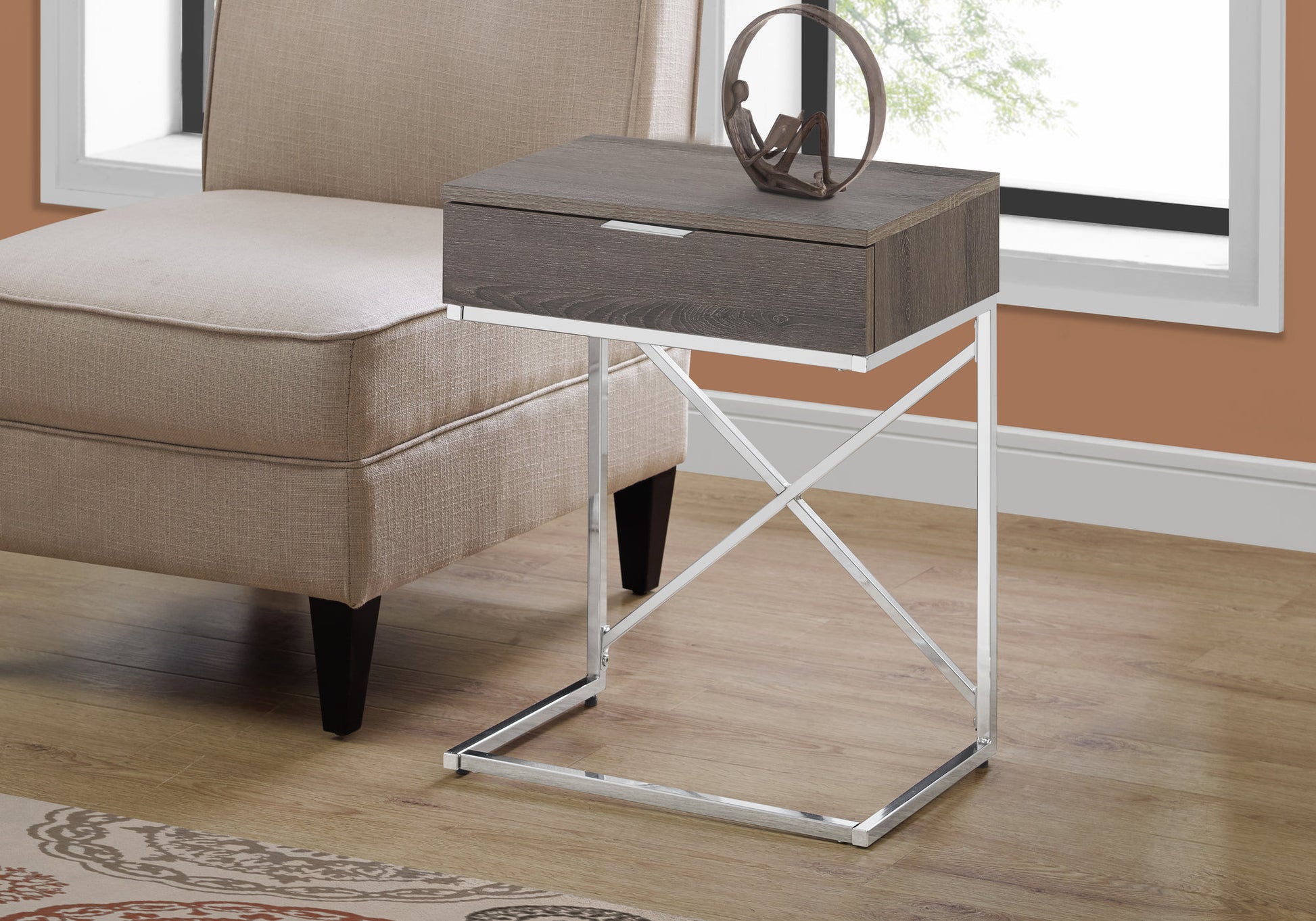 Grey wood end table with single drawer and chrome base beside a beige armchair
