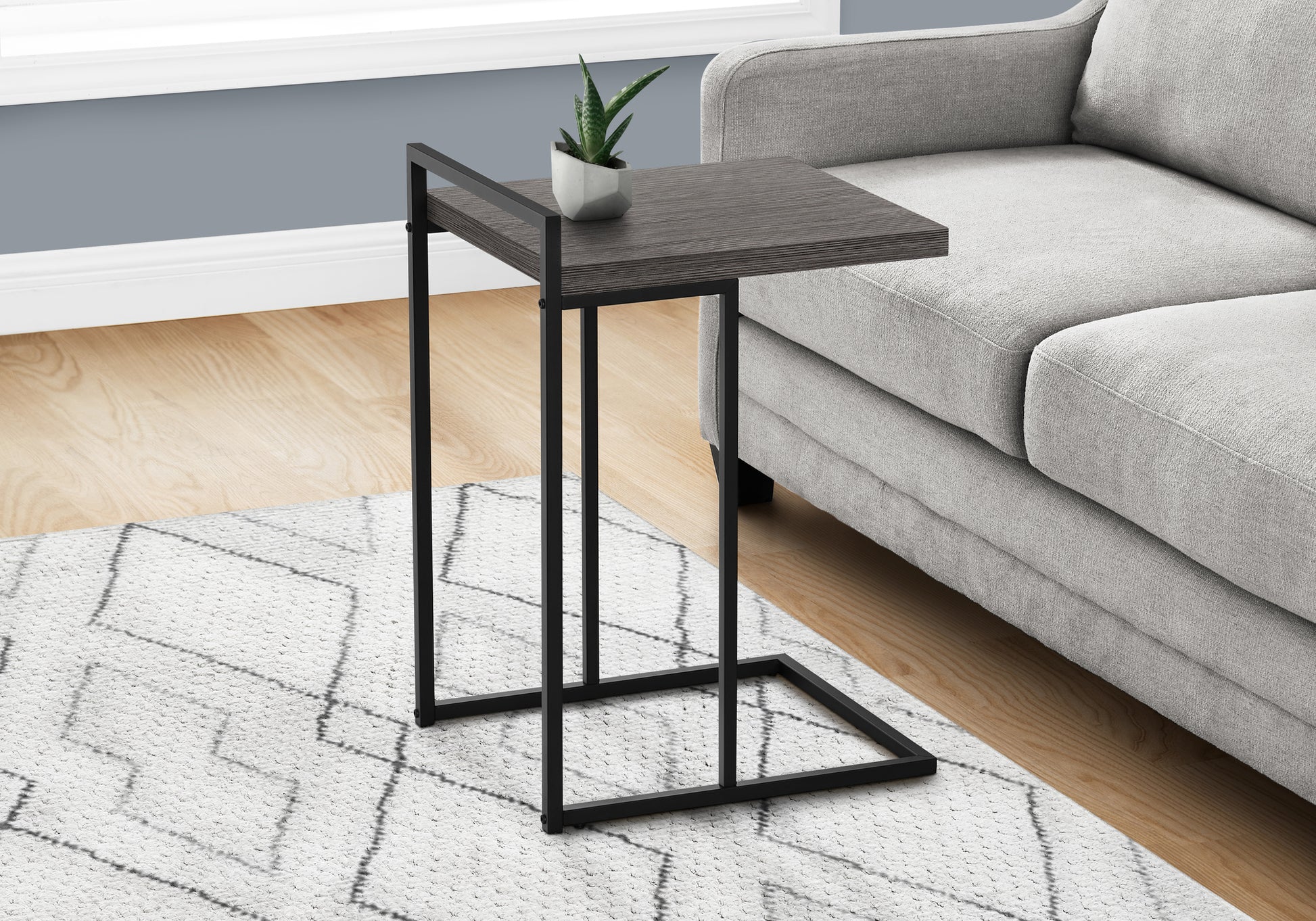 Sleek grey wood grain ctable with black metal frame next to sofa