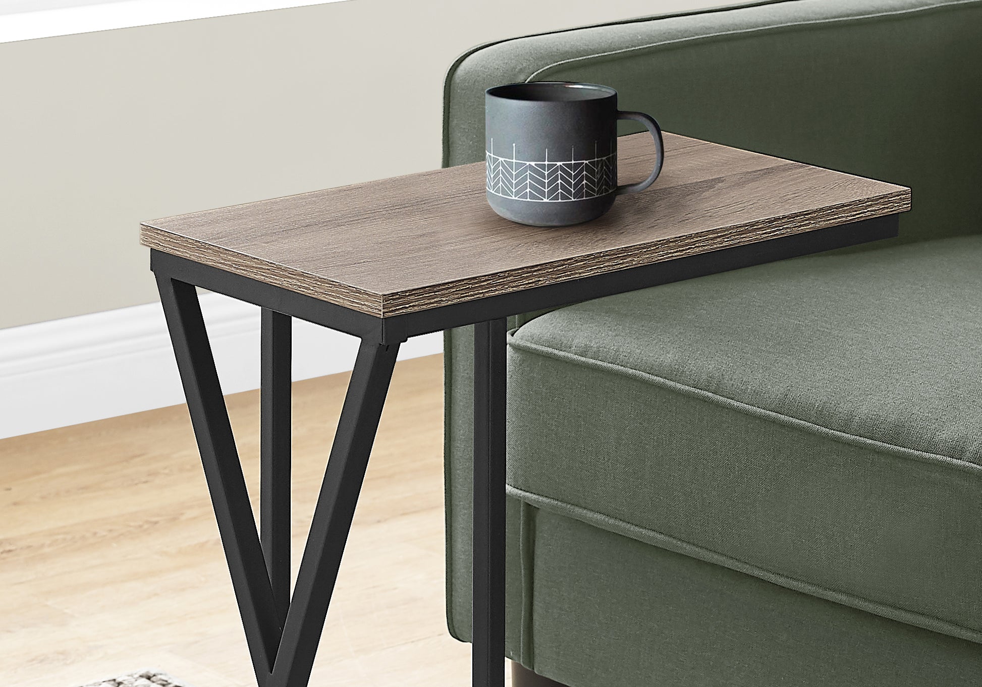 Wood grain Ctable with black metal frame resting on green sofa