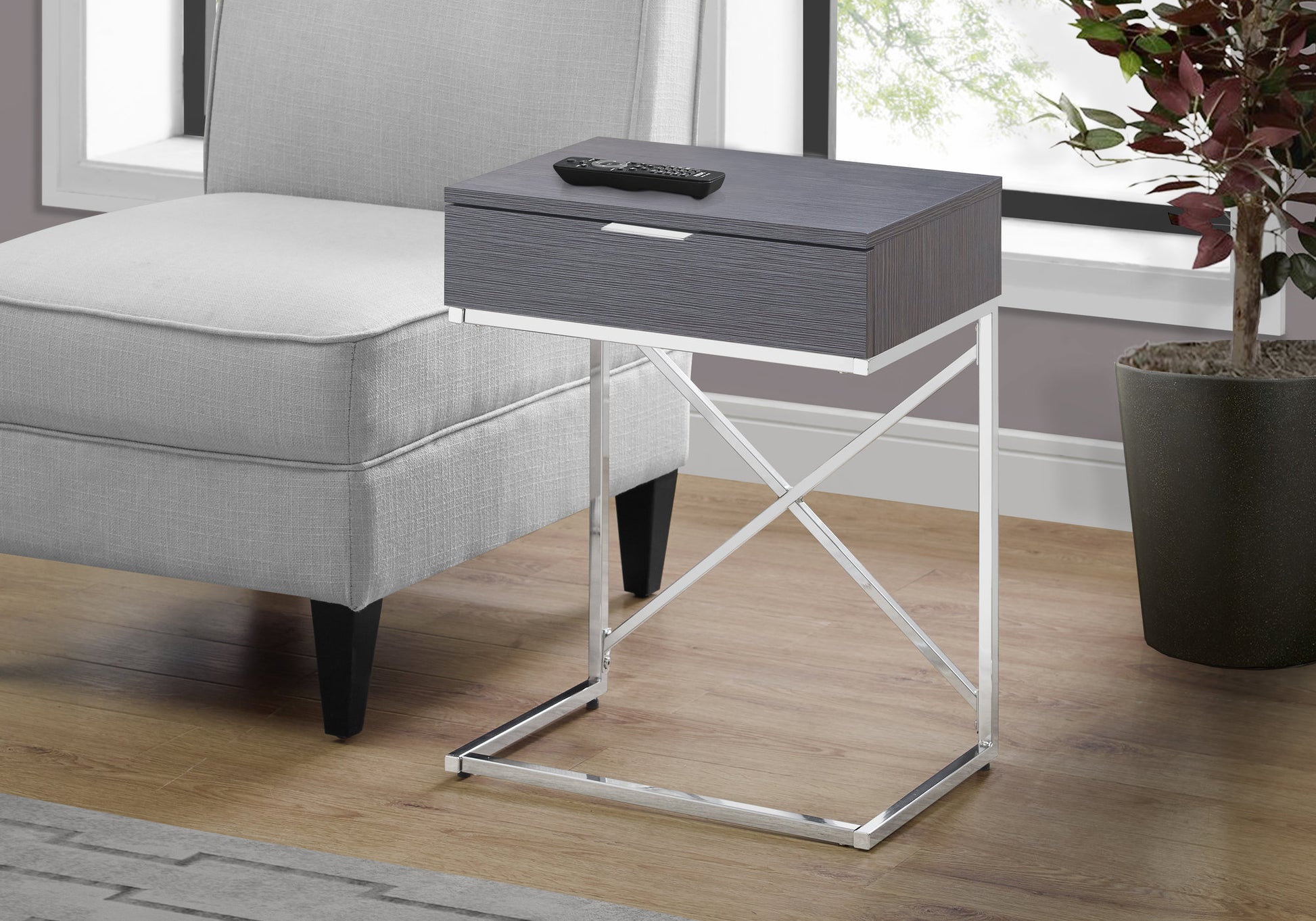 Gray wooden accent table with drawer and chrome base next to armchair