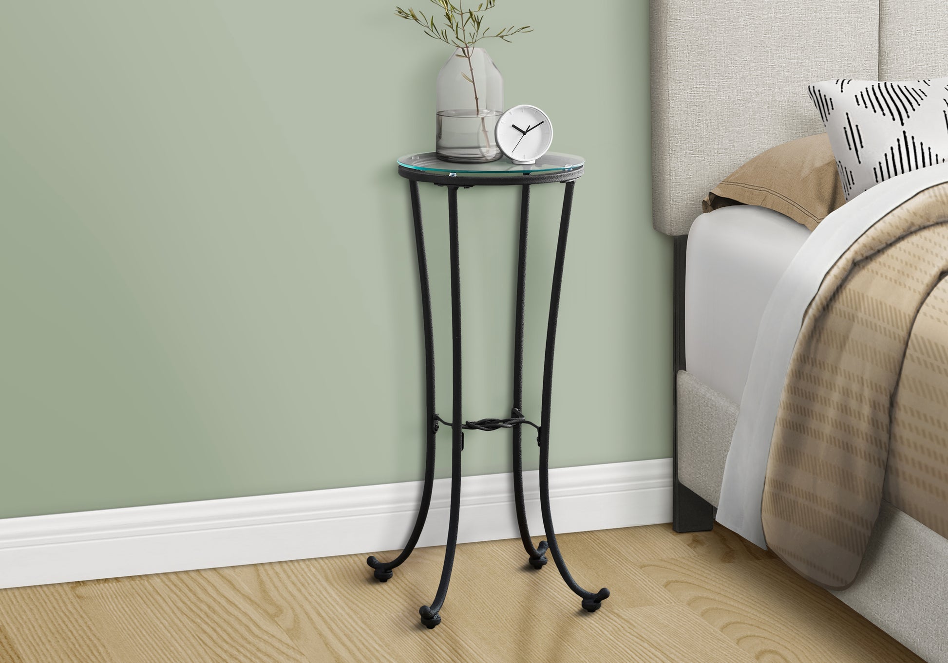 Elegant black metal accent table with clear glass top holding a vase and clock