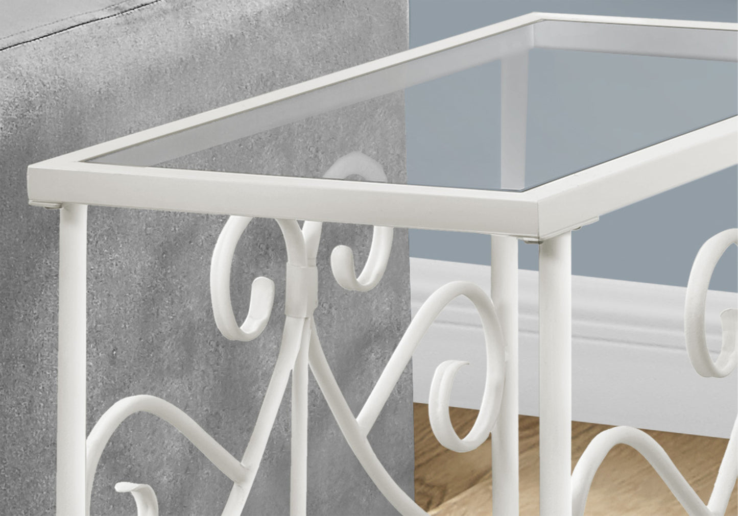 Closeup of a white wrought iron side table with a clear glass top