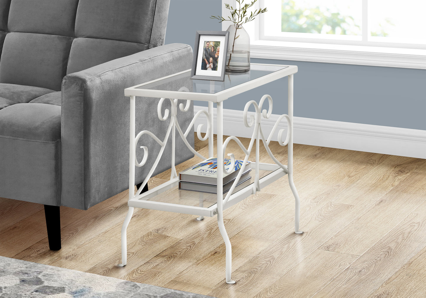 White wrought iron end table with glass top and shelf holding books