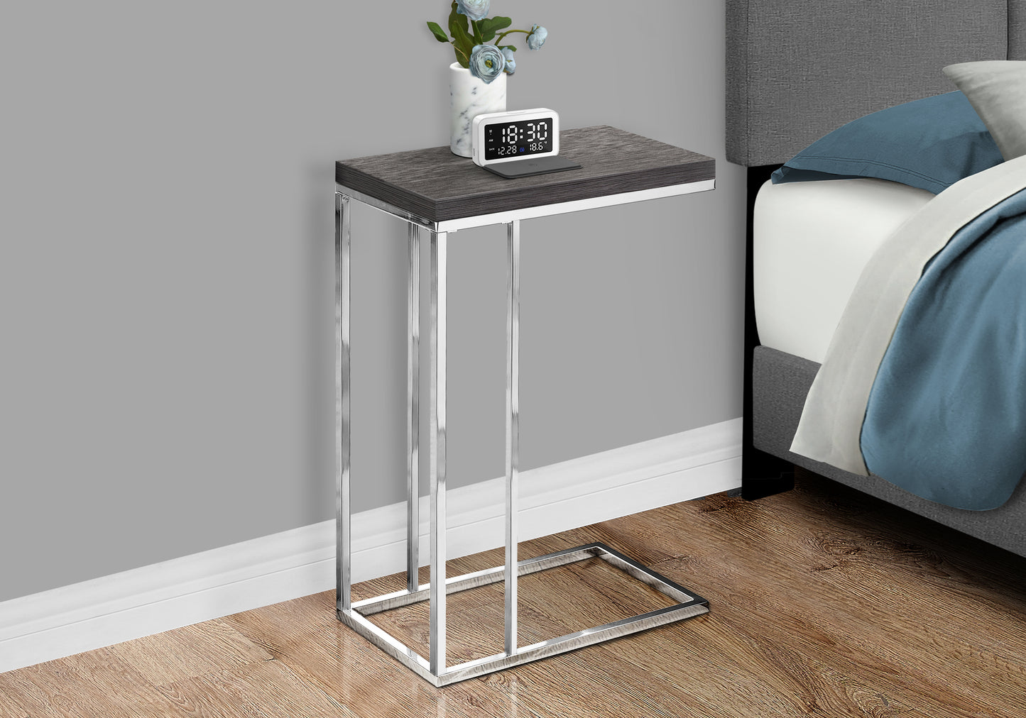 Modern Ctable with dark wood grain top and chrome frame next to a bed
