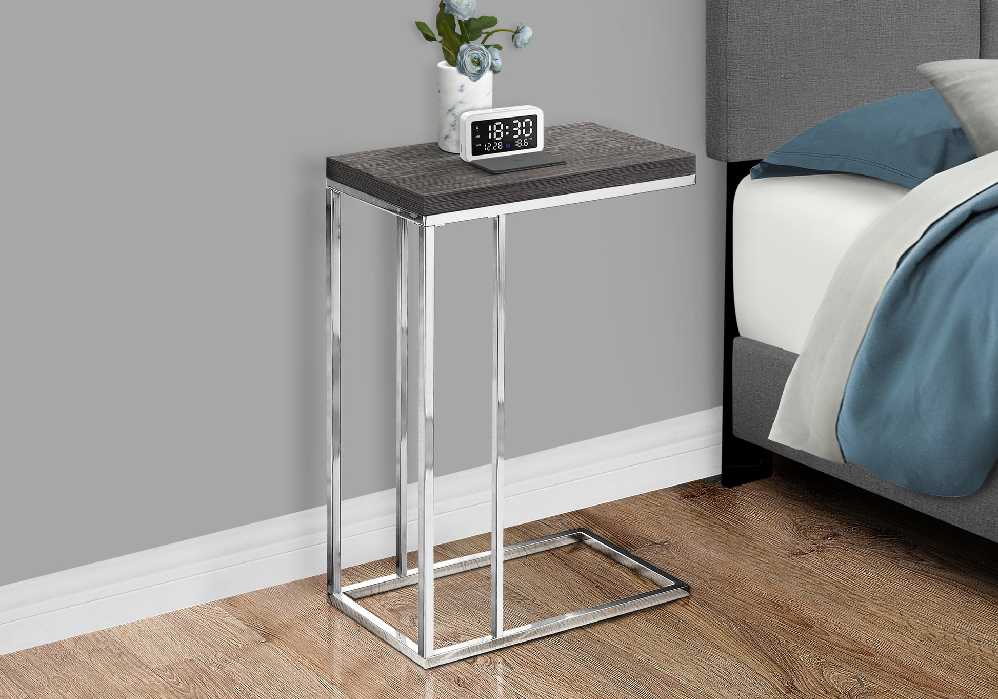 Modern Ctable with dark wood grain top and chrome frame next to a bed