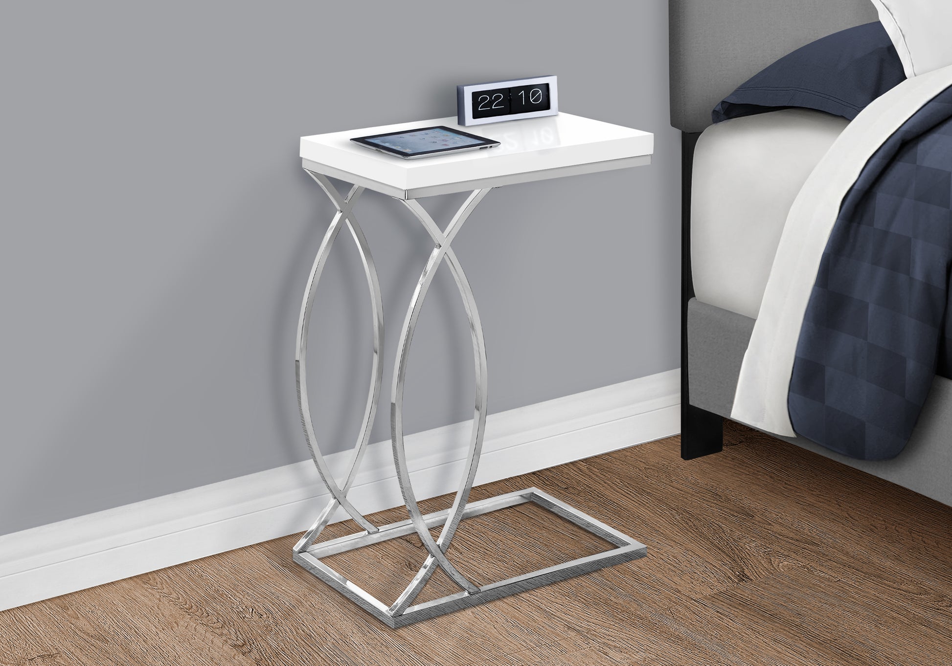 White Cshaped side table with chrome base featuring a tablet and clock