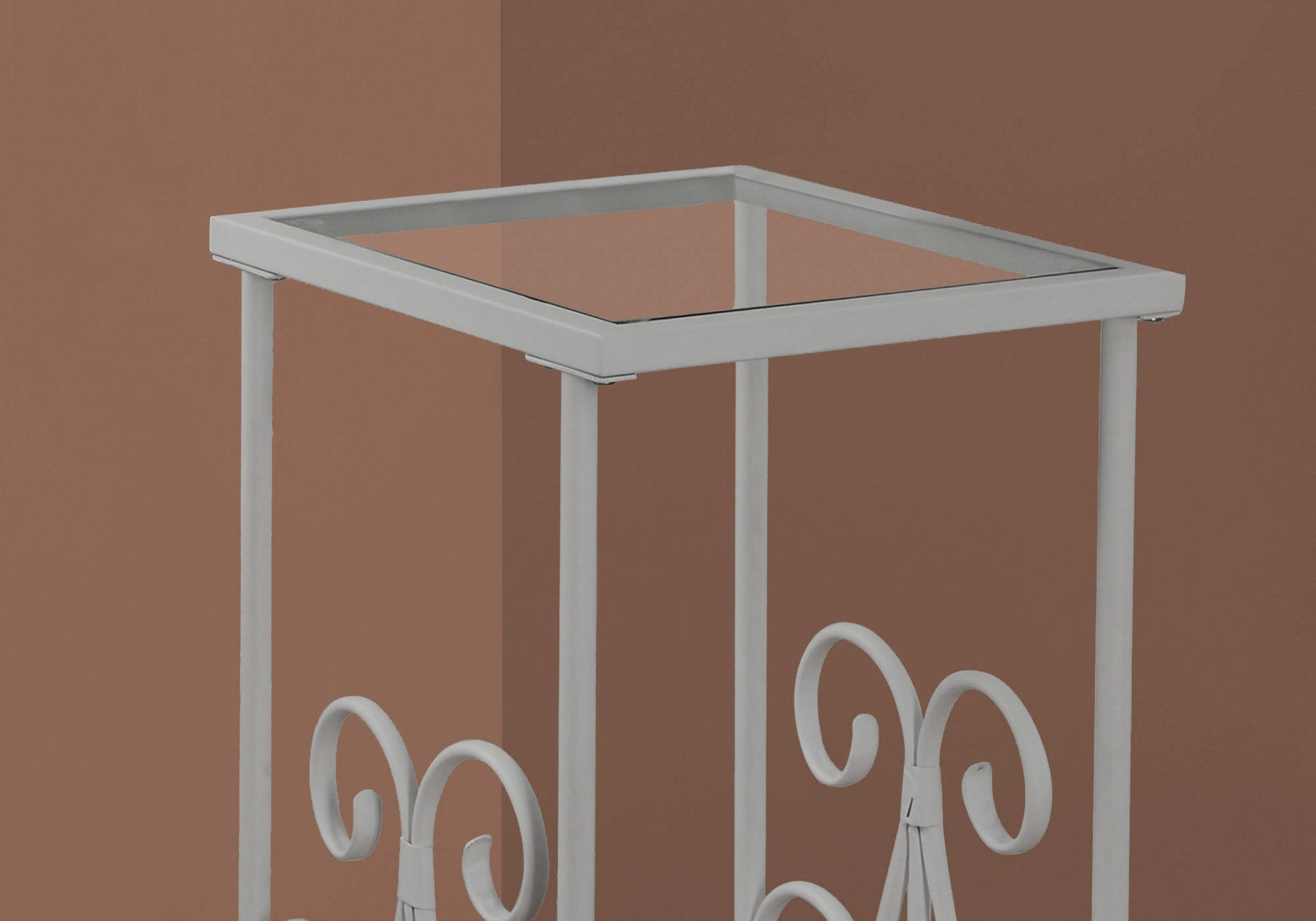White metal plant stand with glass top and ornate scrollwork accents