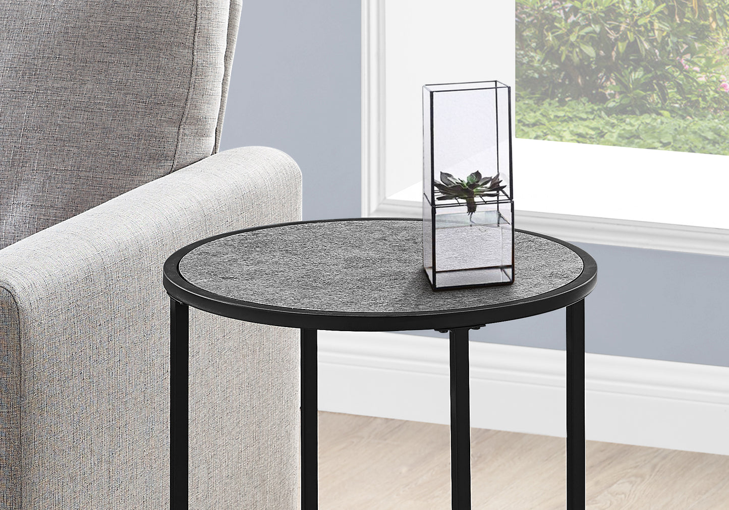 Round stone top side table with black metal legs and a geometric terrarium